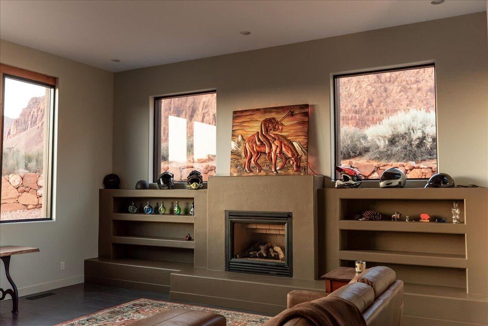 Recessed lighting illuminates a fireplace with a dark metal insert, flanked by integrated shelving and expansive windows showcasing a desert landscape