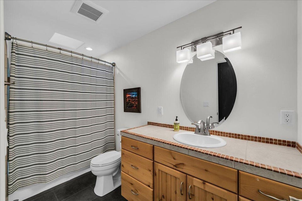 Bathroom featuring a wood-finish vanity with an integrated sink, a tiled countertop with a mosaic trim, and a contemporary light fixture