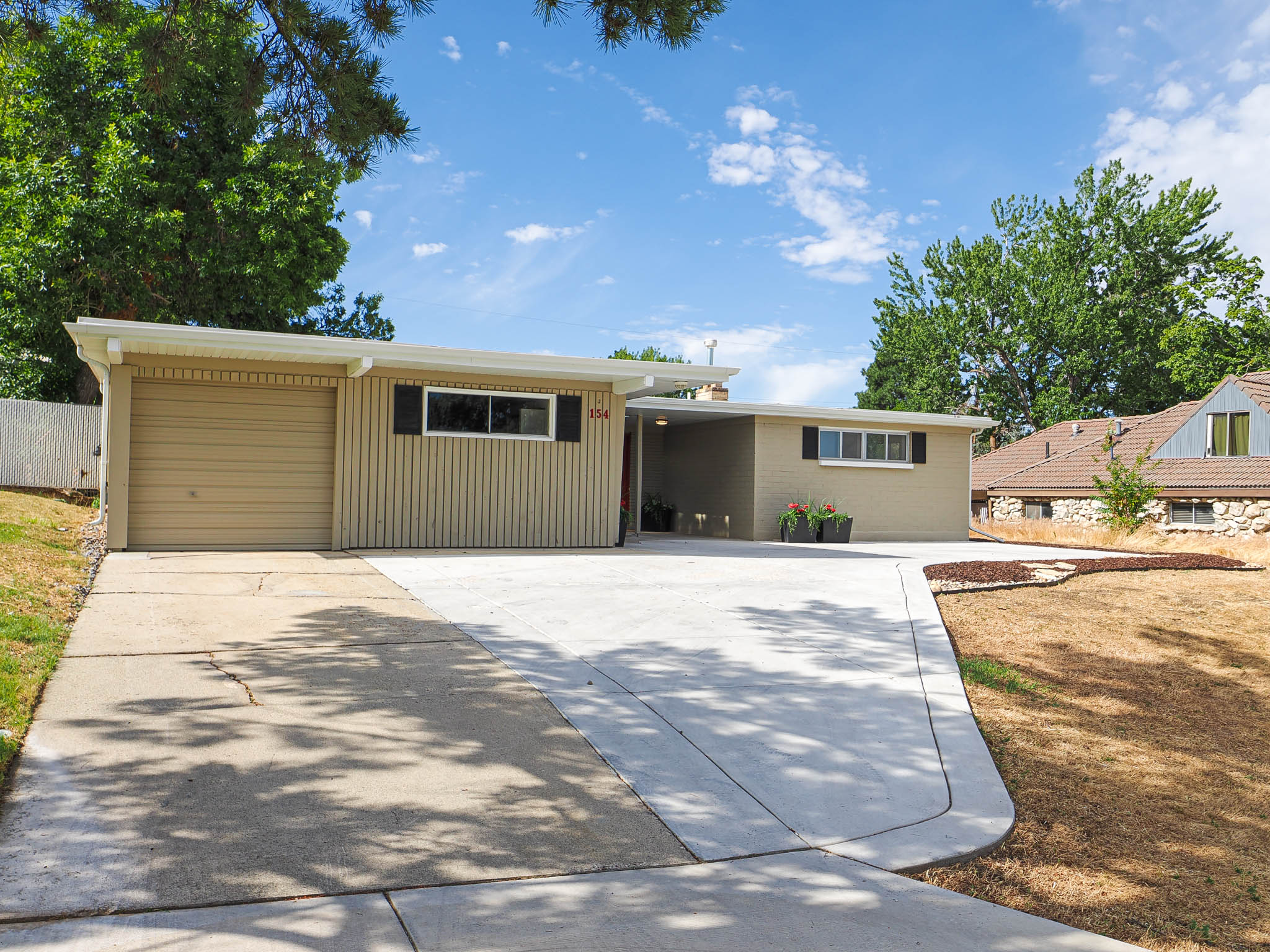 Contemporary ranch-style property featuring a stucco and vertical siding exterior, an attached garage, a carport, and a concrete driveway