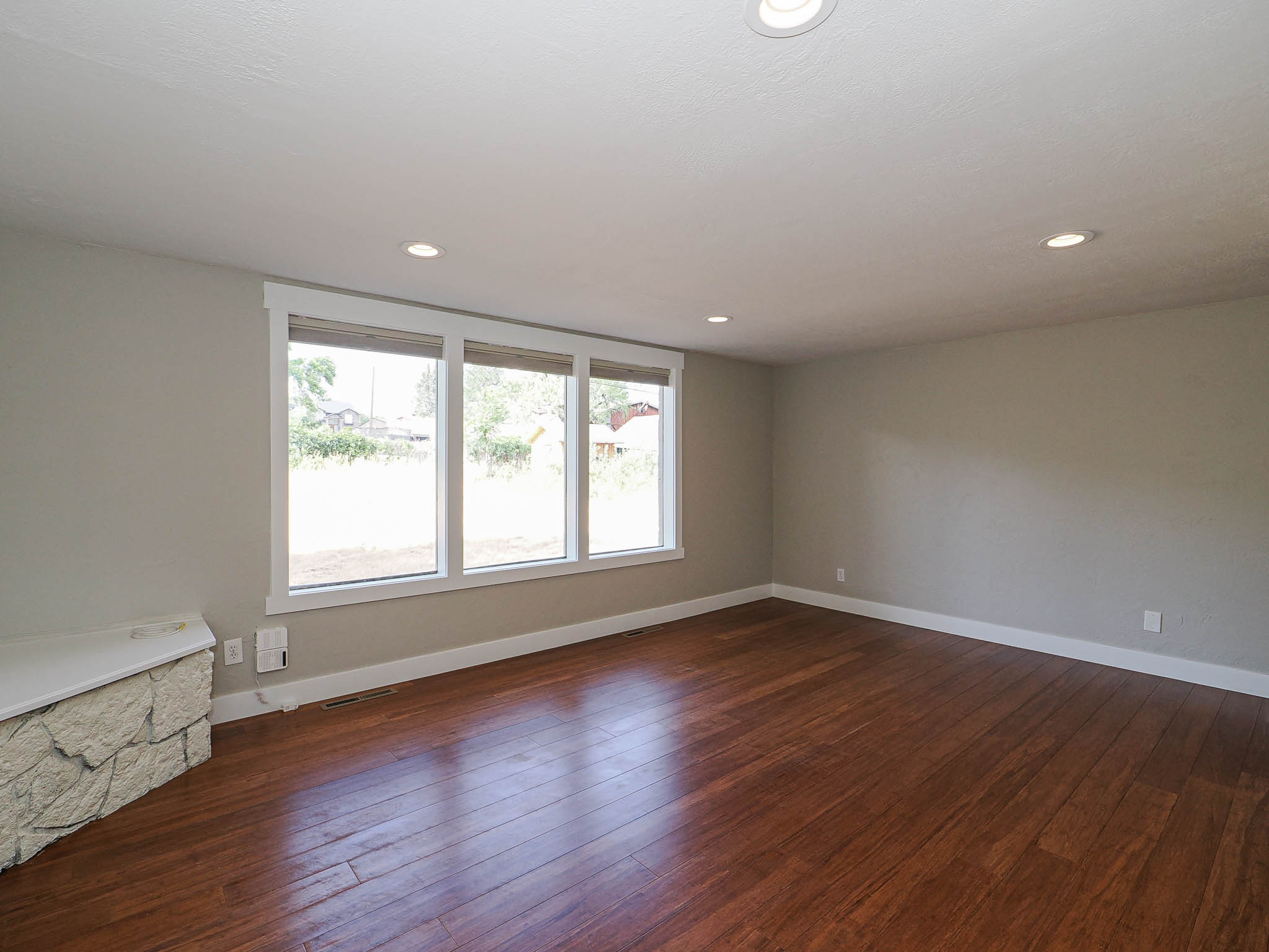 Spacious room featuring rich wood-finish flooring, a three-panel window ensemble, recessed ceiling lighting, a stone-front built-in bench, and neutral wall tones