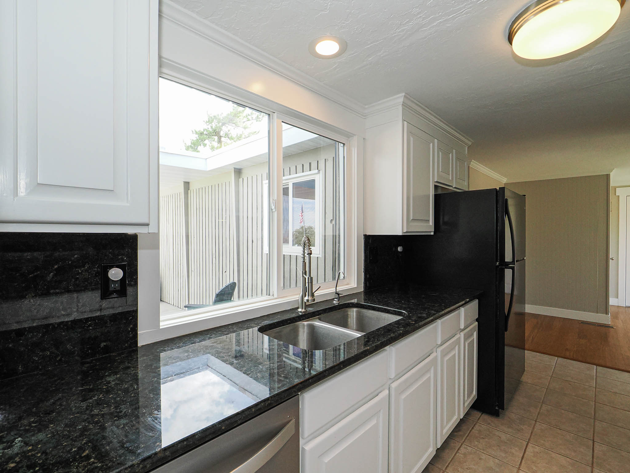 Kitchen featuring a stainless steel double sink with a gooseneck faucet, dark countertops, white cabinetry with crown molding, and a black refrigerator