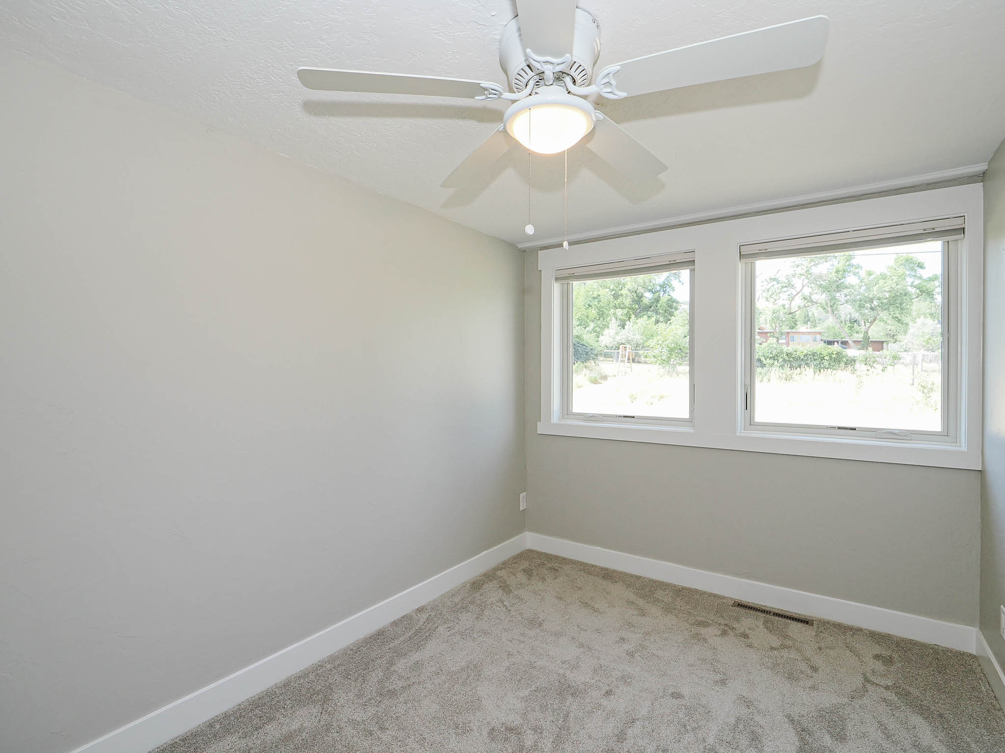 Room featuring light neutral wall paint, two large windows with white trim, a ceiling fan with integrated lighting, and gray carpeting