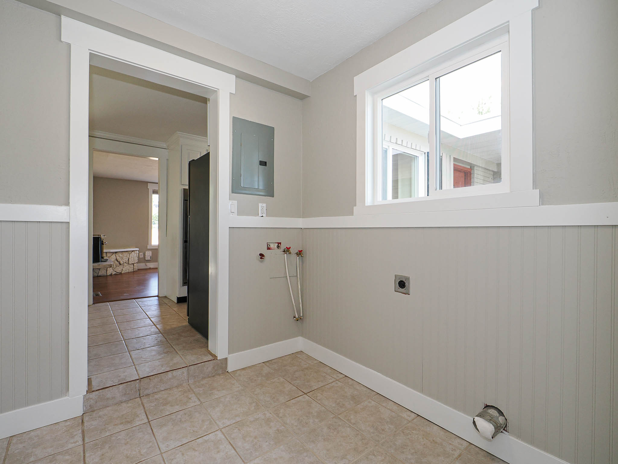 Utility room featuring tile flooring, wainscoting, a double-pane window, and a finished doorway