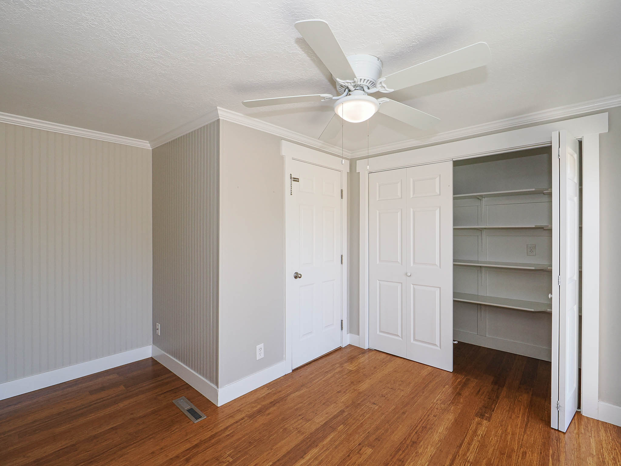 Room featuring wood-finish flooring, a ceiling fan with integrated lighting, and crown molding