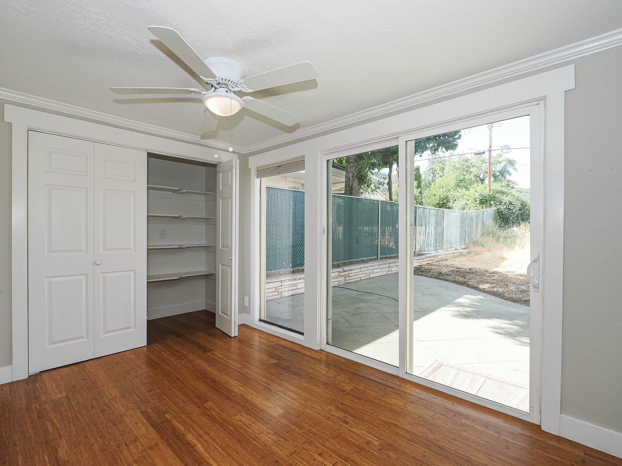 Room featuring wood-finish flooring, a ceiling fan with integrated lighting, and a closet with bifold doors and built-in shelving