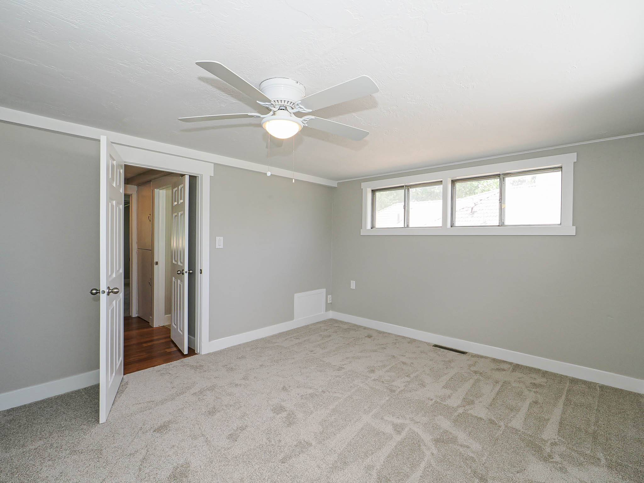 Neutral-toned room featuring a white ceiling fan with integrated lighting, multiple windows with white trim, and plush carpeting