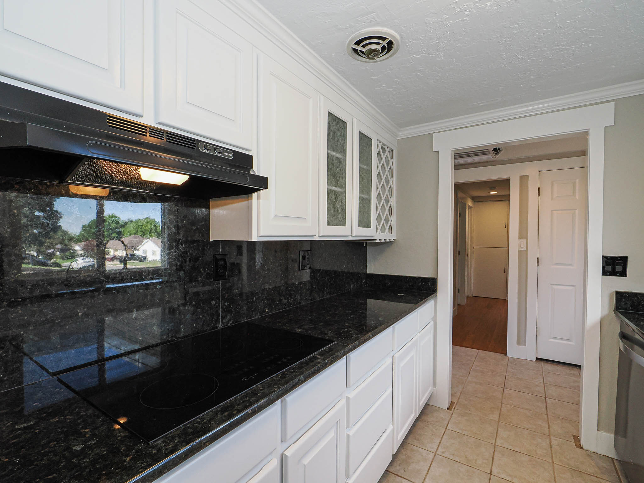 Kitchen featuring white paneled cabinetry with some glass-front doors, black cooktop, dark speckled countertops, and a matching backsplash