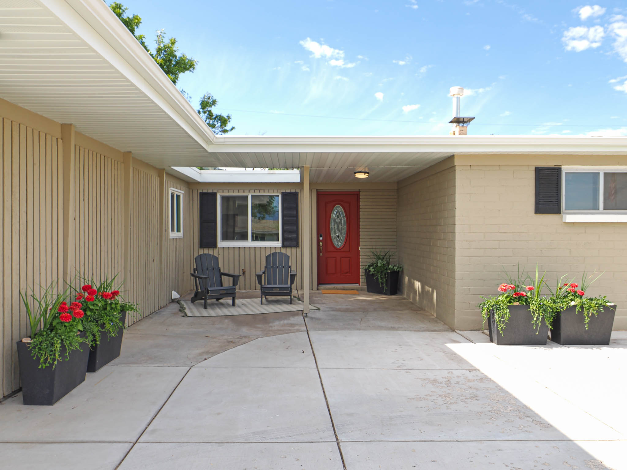 Covered front entry featuring a red paneled door with an oval glass insert, brick exterior, wood-paneled siding, and a concrete driveway