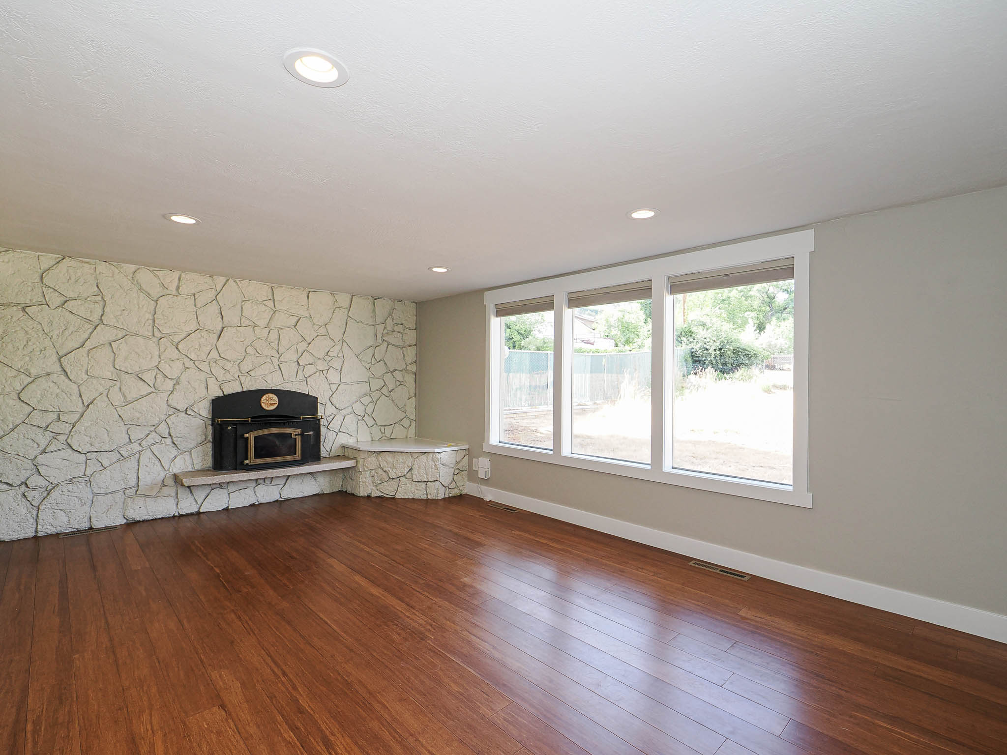 Spacious living area featuring rich wood-finish flooring, a stone-clad accent wall with a built-in fireplace, and recessed ceiling lighting