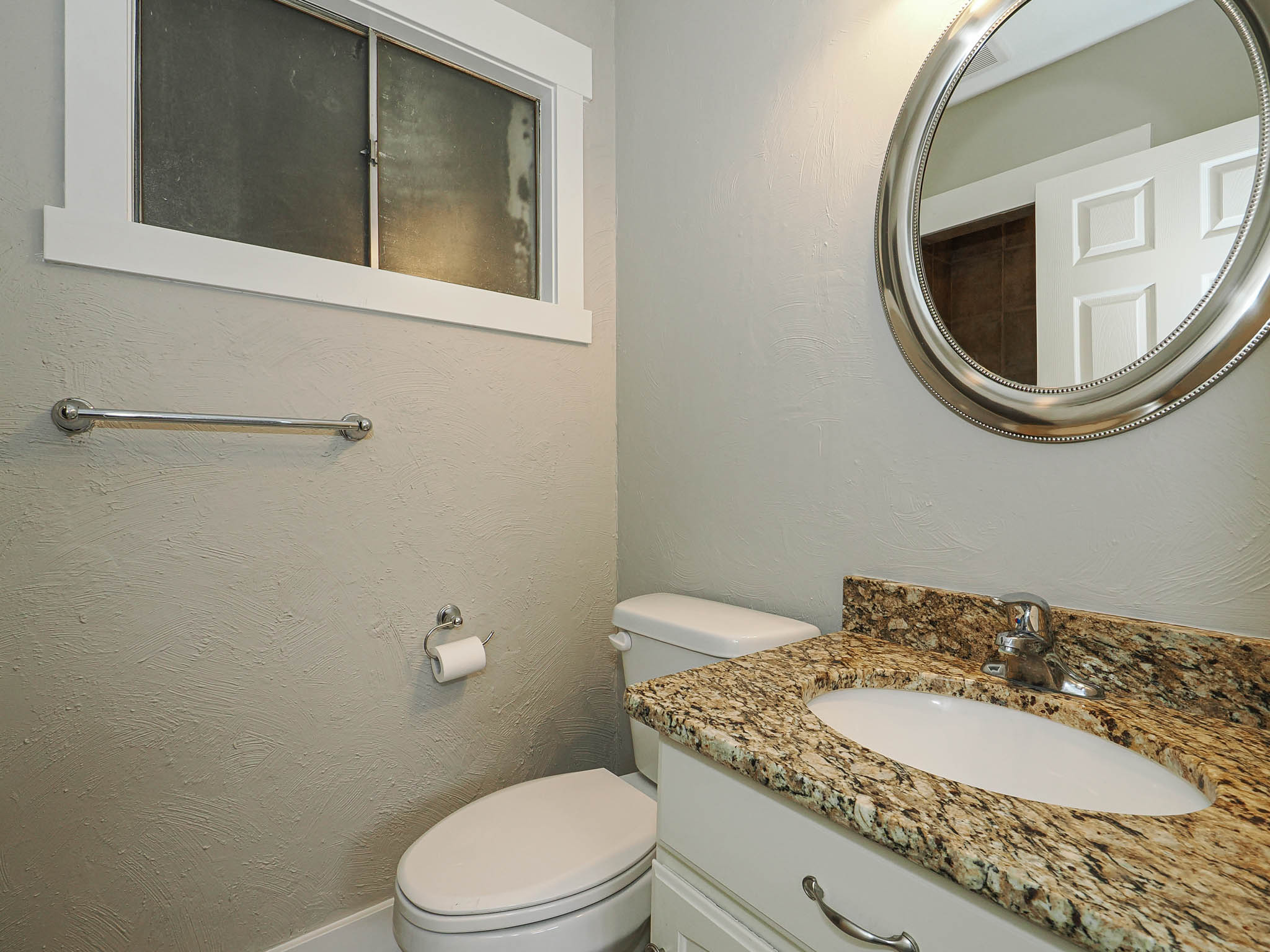 Powder room featuring a granite-style countertop, white vanity with cabinet storage, oval mirror, and a window with frosted glass