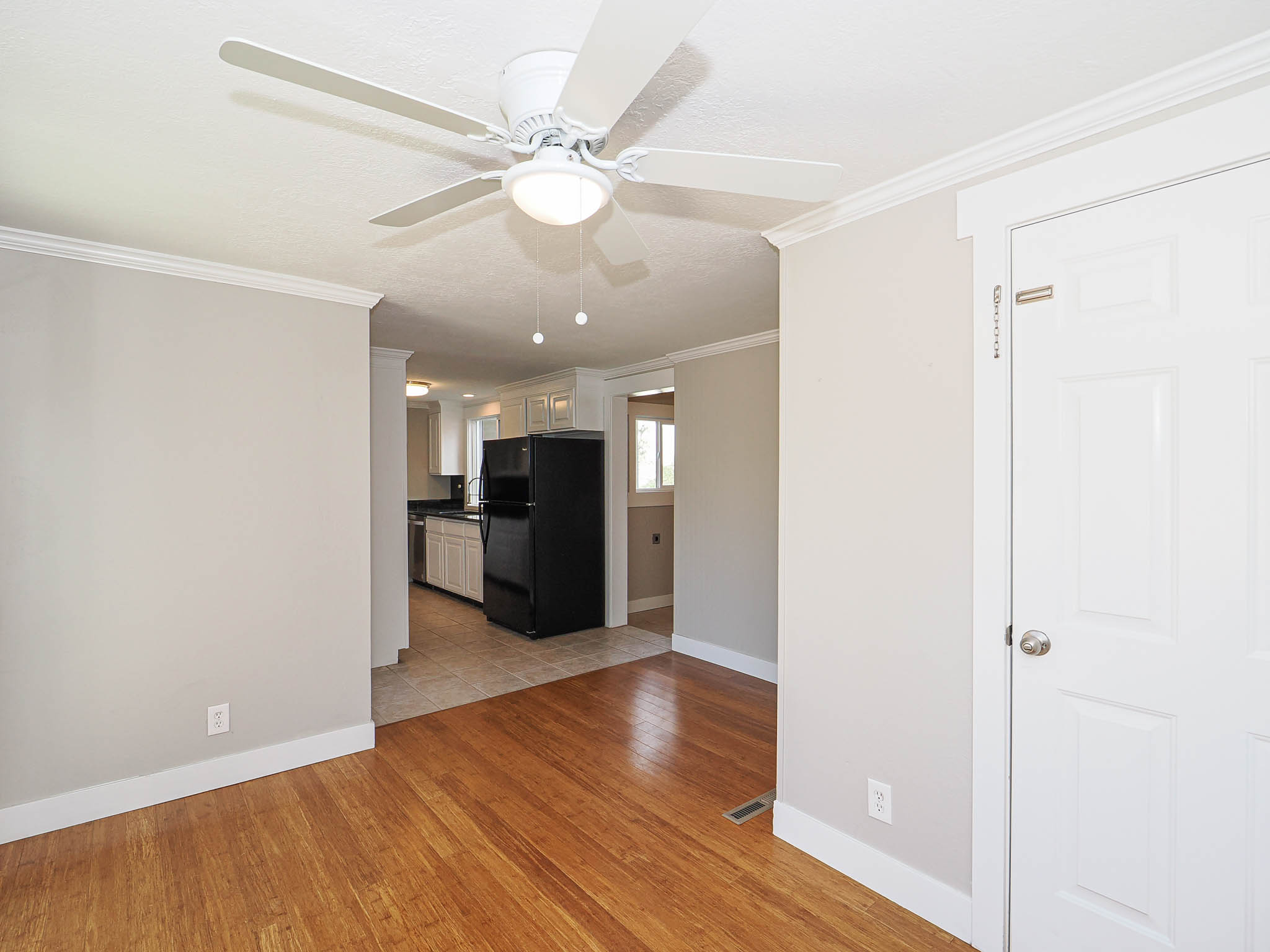 Bright interior space with wood-finish flooring, a ceiling fan with integrated lighting, and a white paneled door