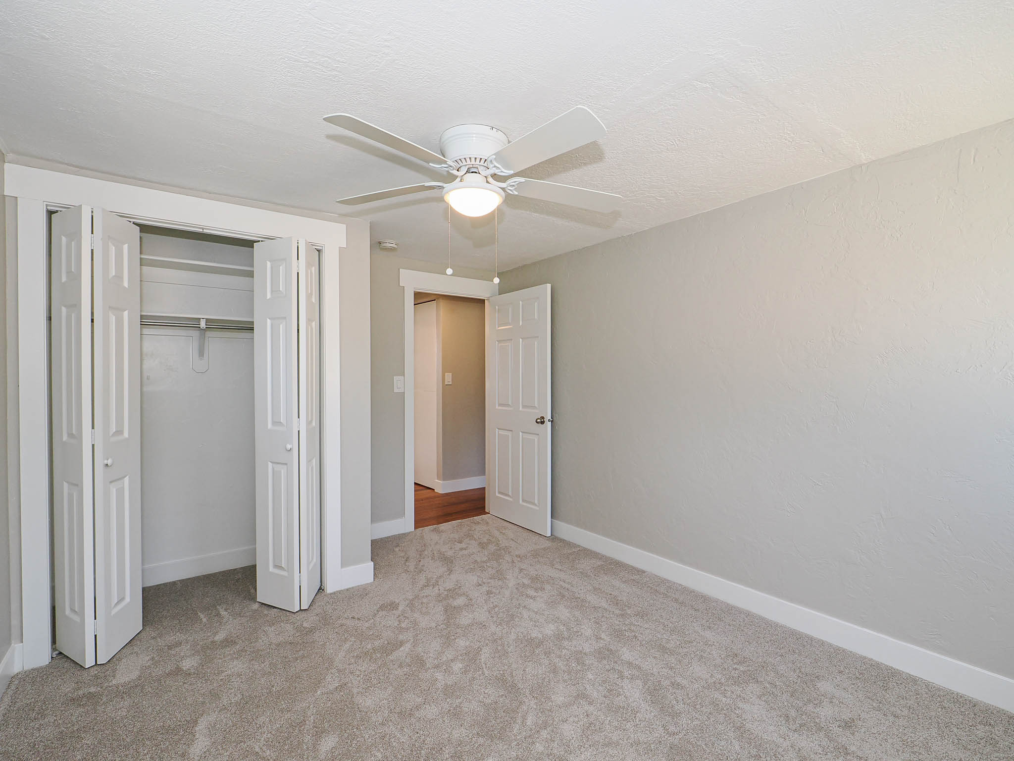 Carpeted room featuring a ceiling fan with integrated lighting, bi-fold closet doors, white baseboards, and a white interior door