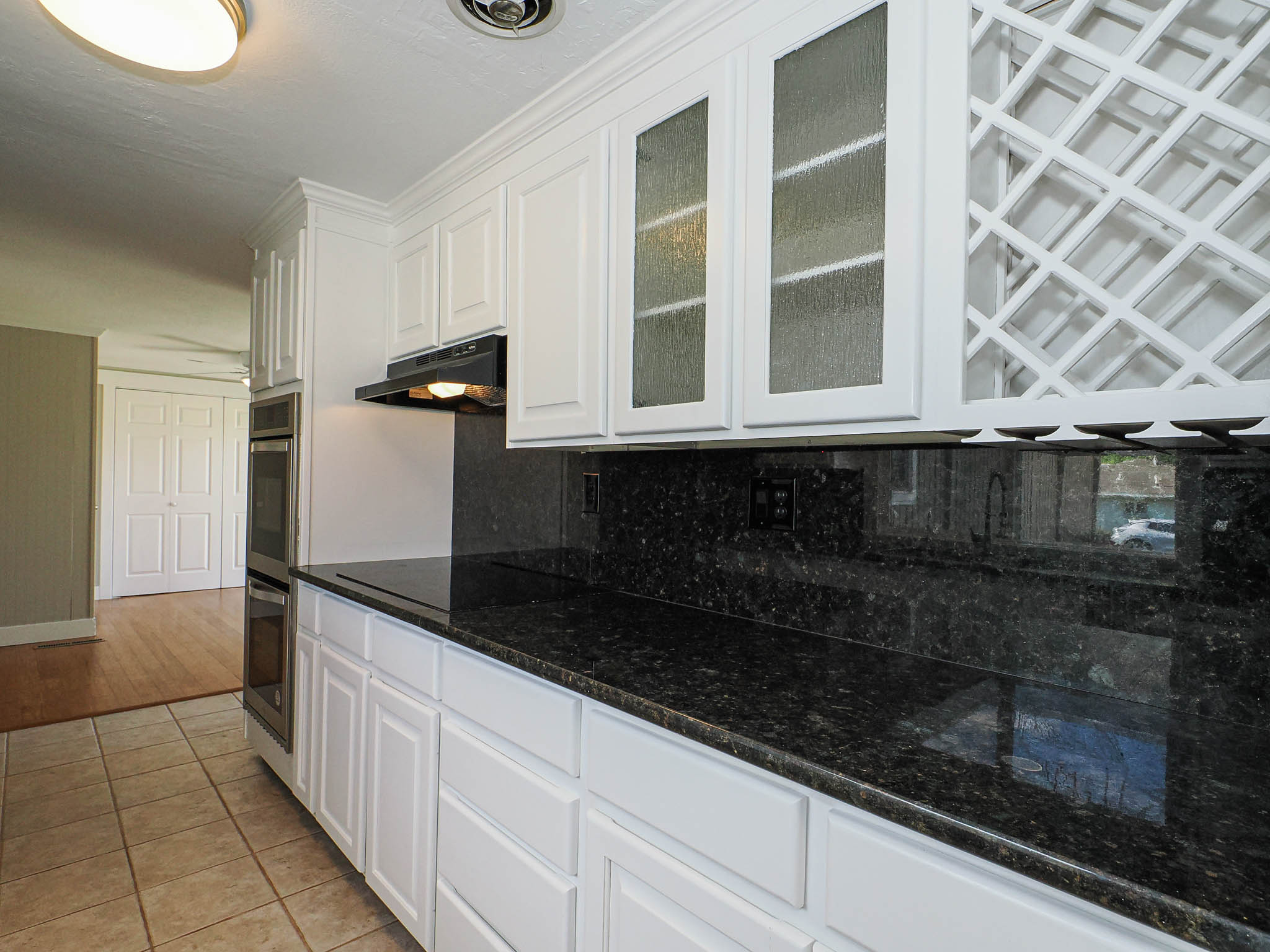 Kitchen featuring white cabinetry, dark speckled countertops, tile flooring, built-in double ovens, and a wine rack