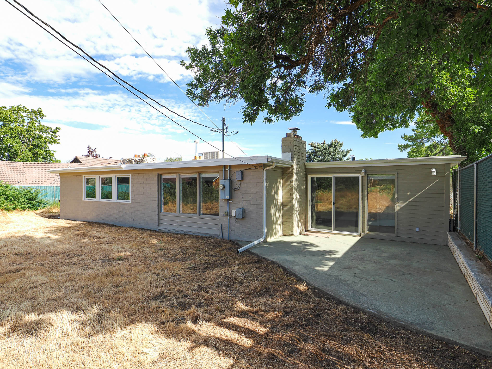 Rear exterior featuring a concrete patio, brick chimney, multiple windows, and sliding glass doors