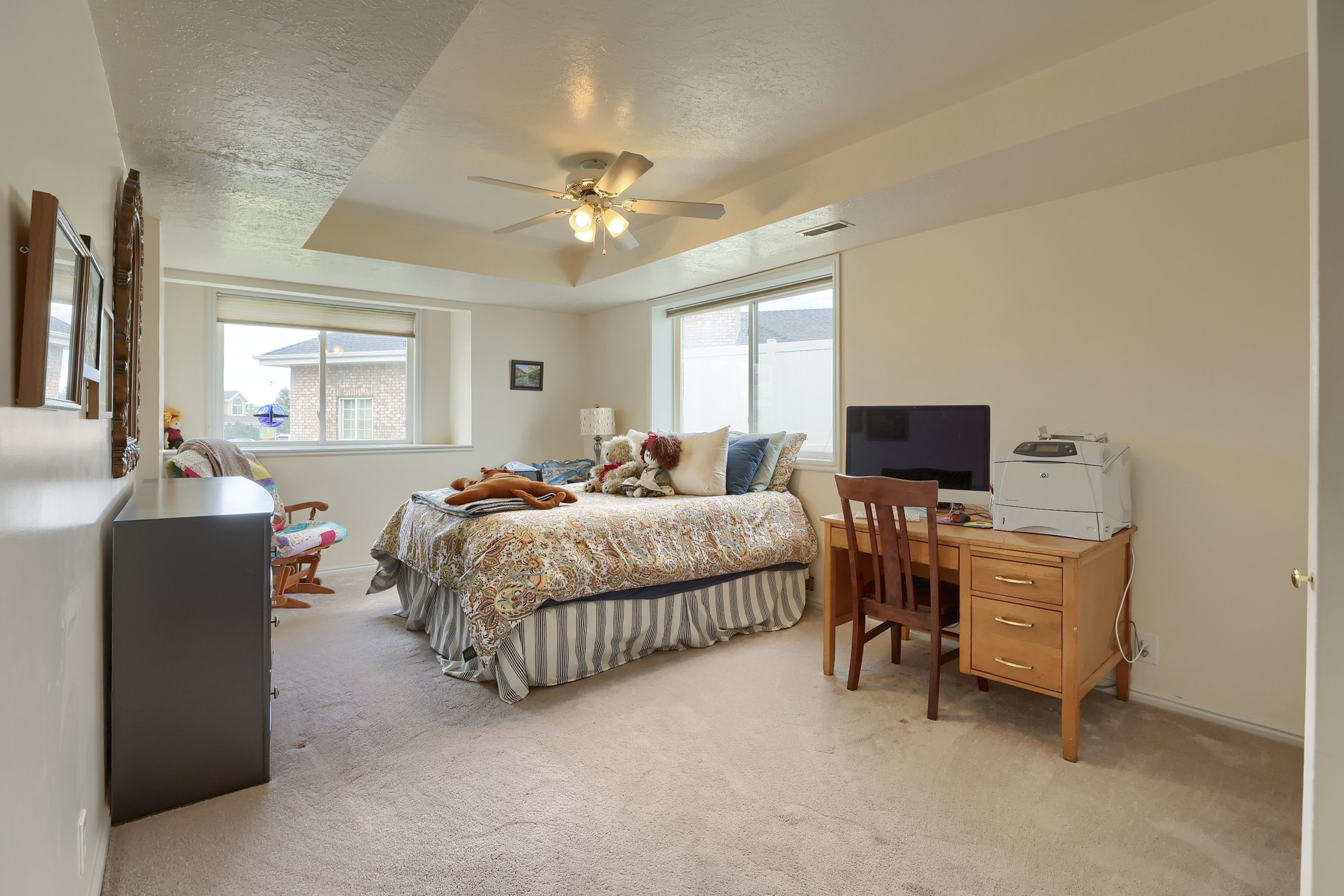 Bedroom featuring a tray ceiling with a ceiling fan, two large windows, carpet flooring, and neutral wall tones