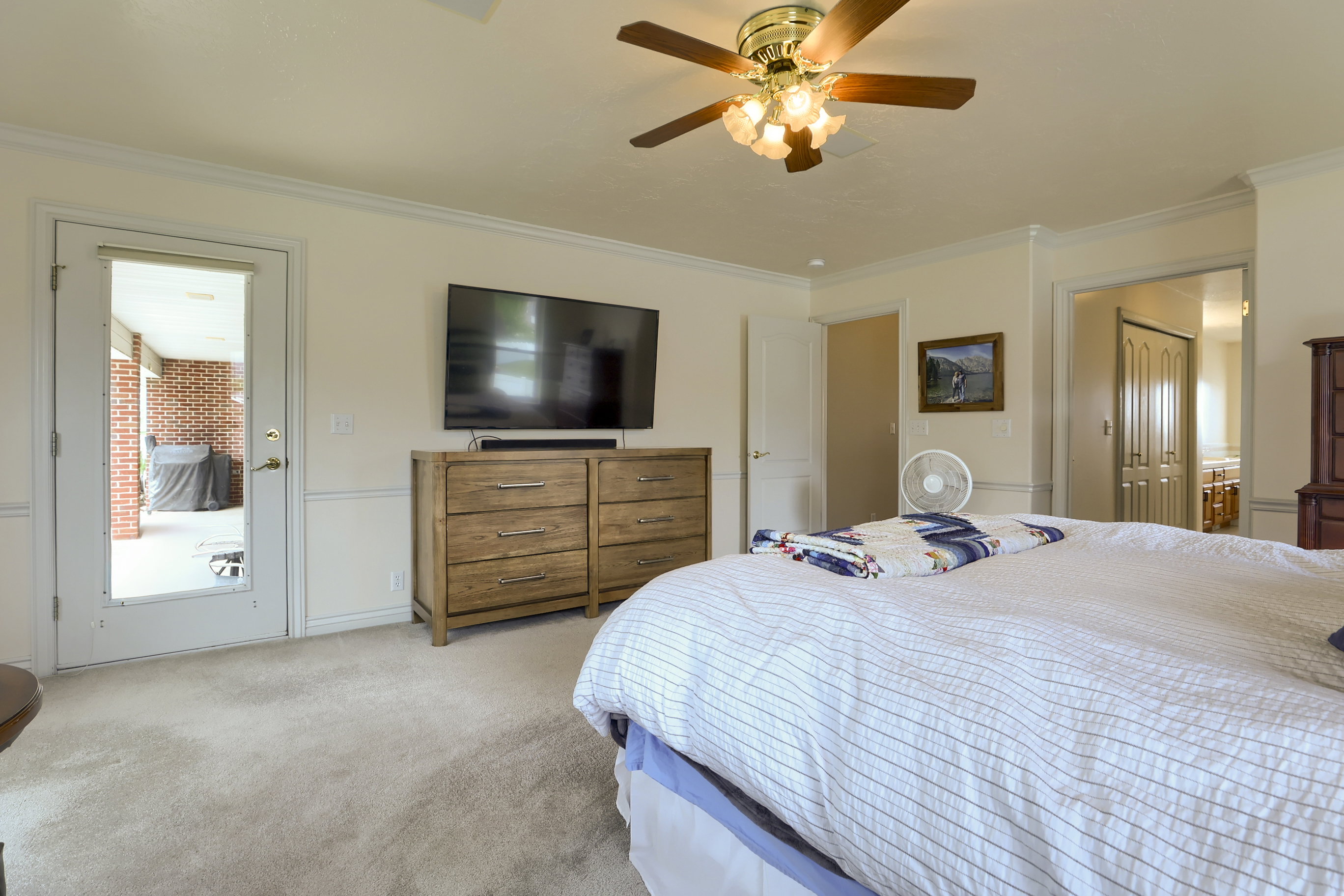 Carpeted room featuring a ceiling fan with integrated lighting, crown molding, and a paneled door leading to an outdoor area with brickwork