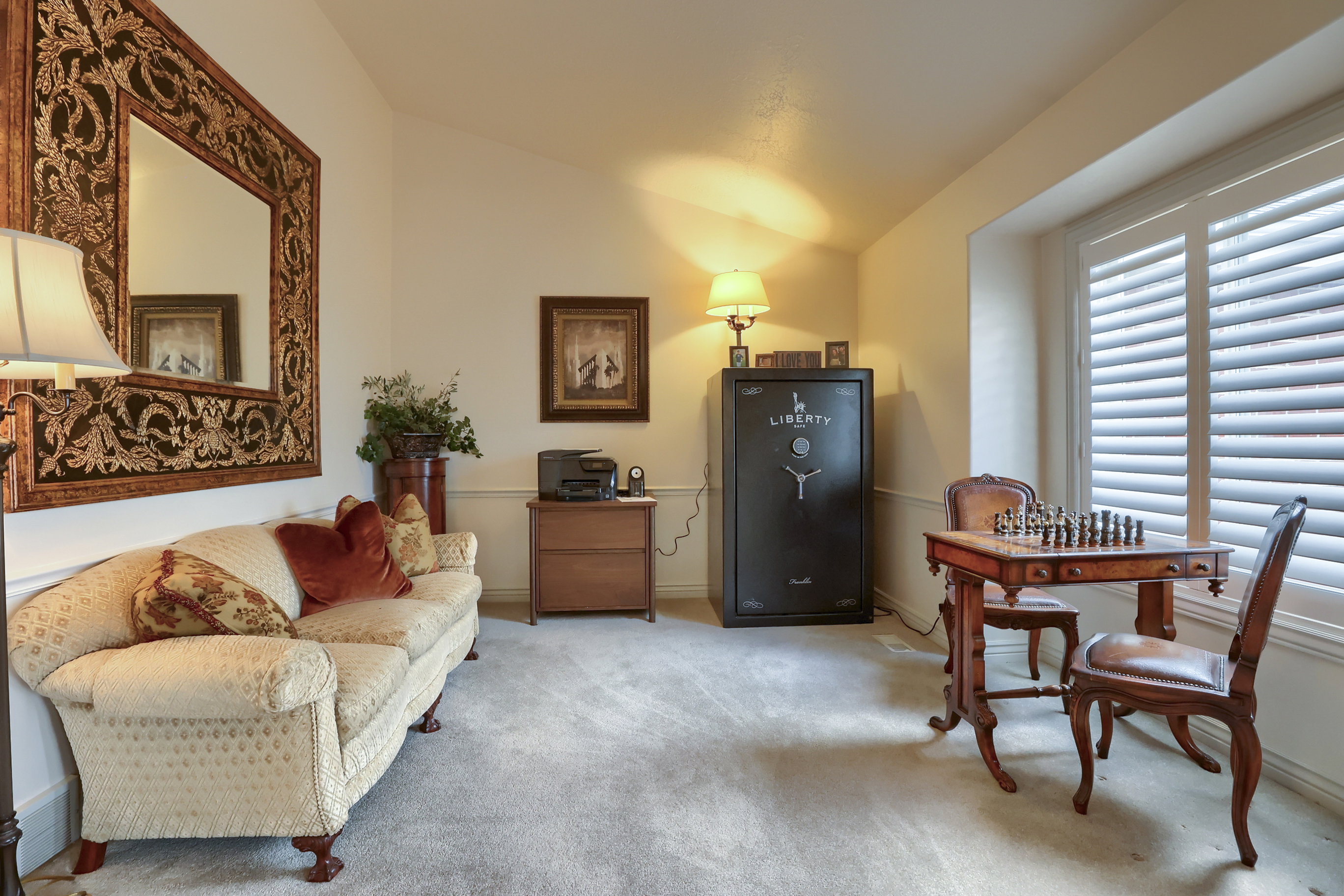 Carpeted room with a vaulted ceiling, featuring plantation shutters on a large window, decorative crown molding, and a built-in safe