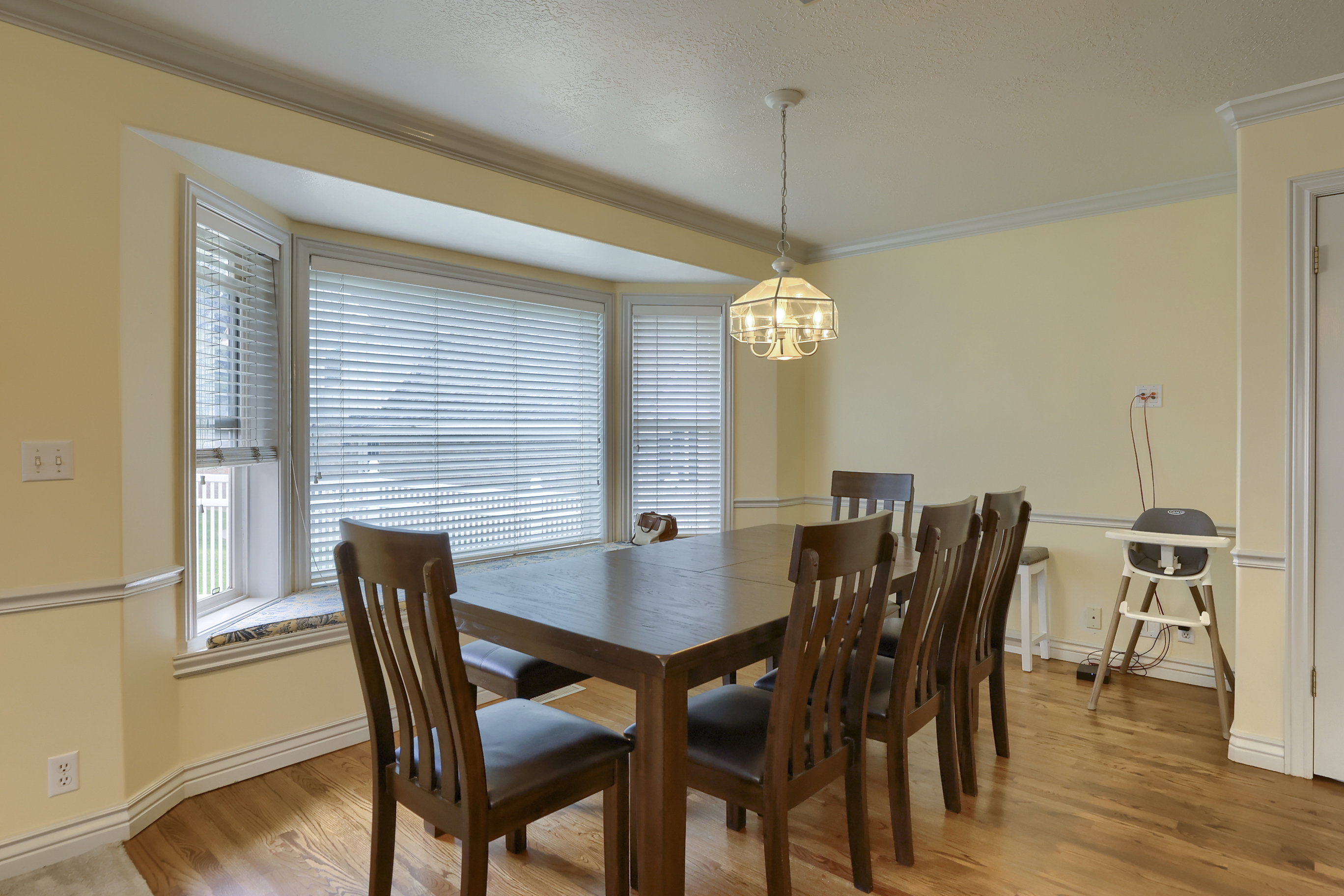 Dining area featuring a bay window, hardwood flooring, a ceiling-mounted chandelier, and crown molding