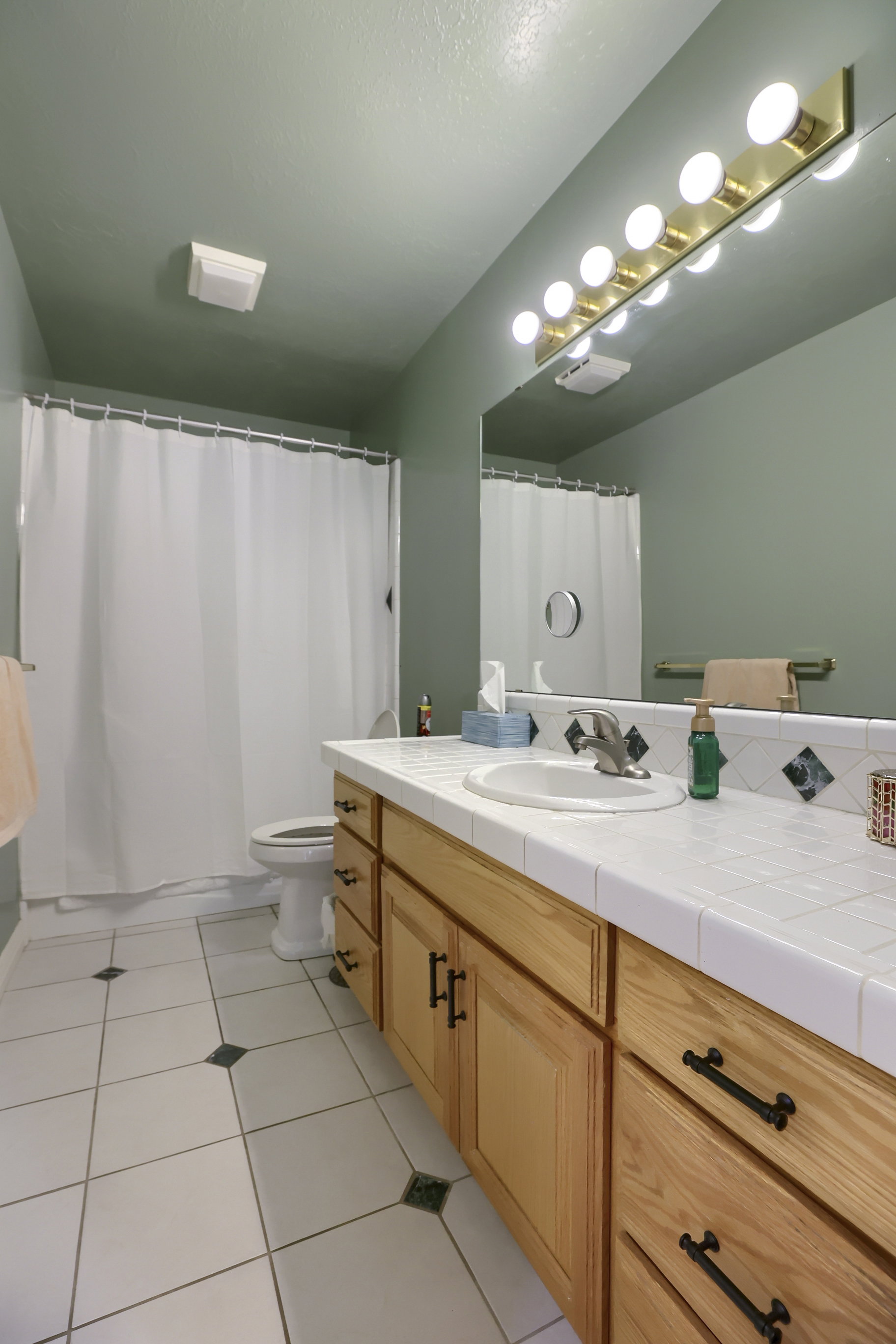 Bathroom featuring a wood-finish vanity with ample storage, white tile countertop, and a large wall-mounted mirror