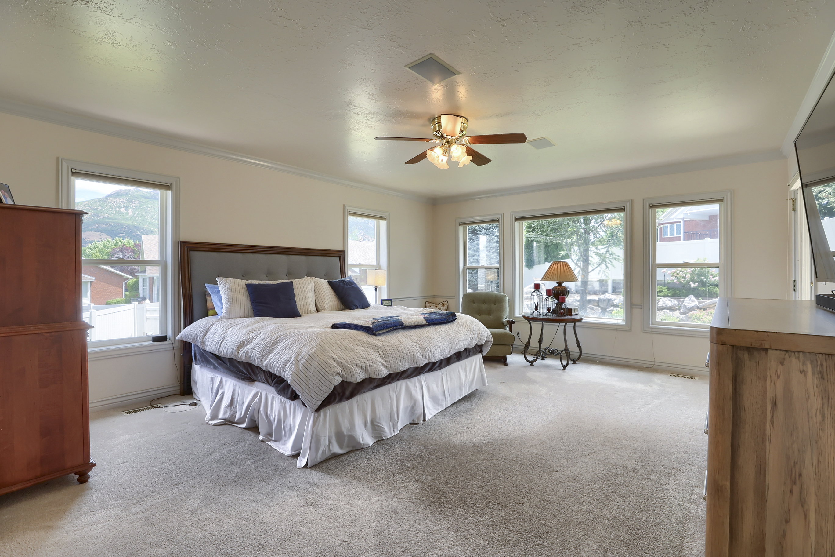Spacious room featuring neutral carpet flooring, multiple windows, a ceiling fan with integrated lighting, and crown molding