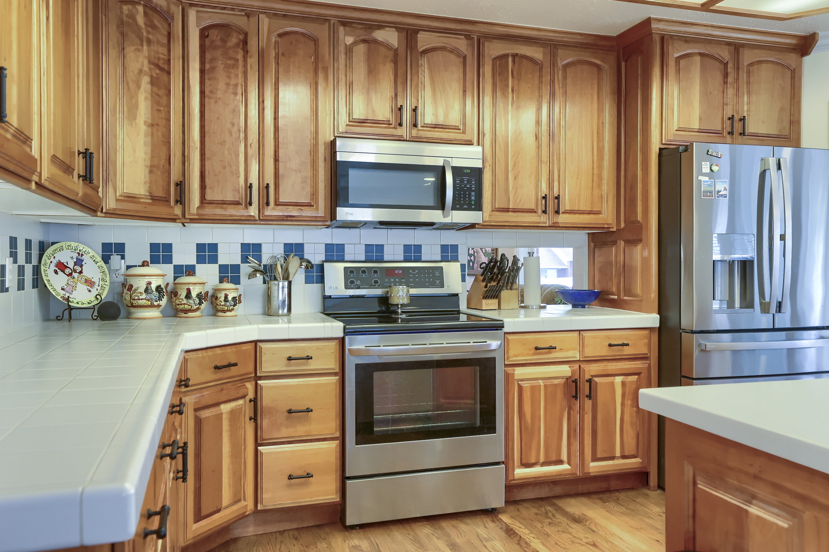 Kitchen featuring wood cabinetry, stainless steel appliances, tile countertops, a tiled backsplash, and wood-finish flooring