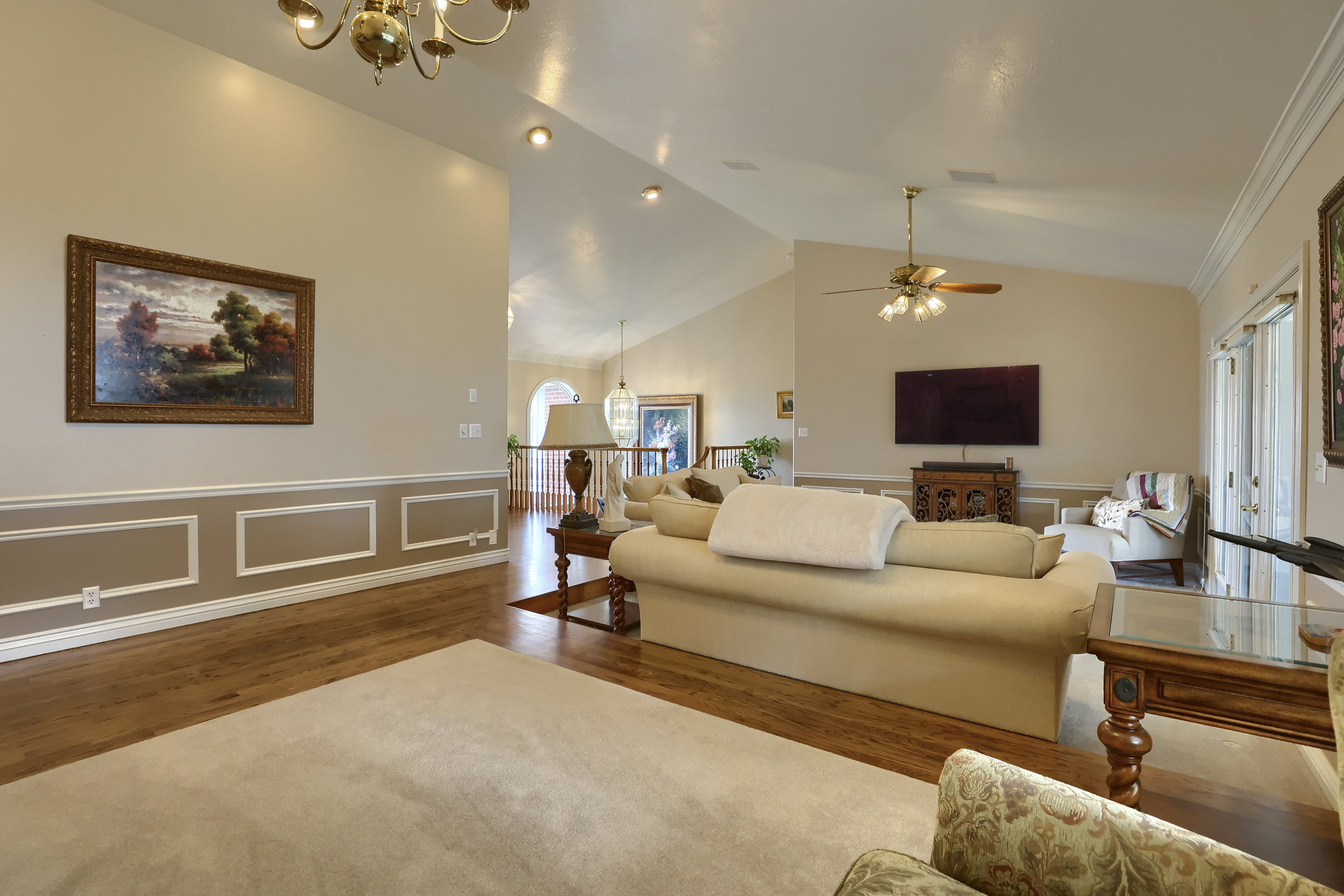 Living room featuring wood-finish flooring, vaulted ceilings, recessed lighting, and chair rail molding with decorative paneling