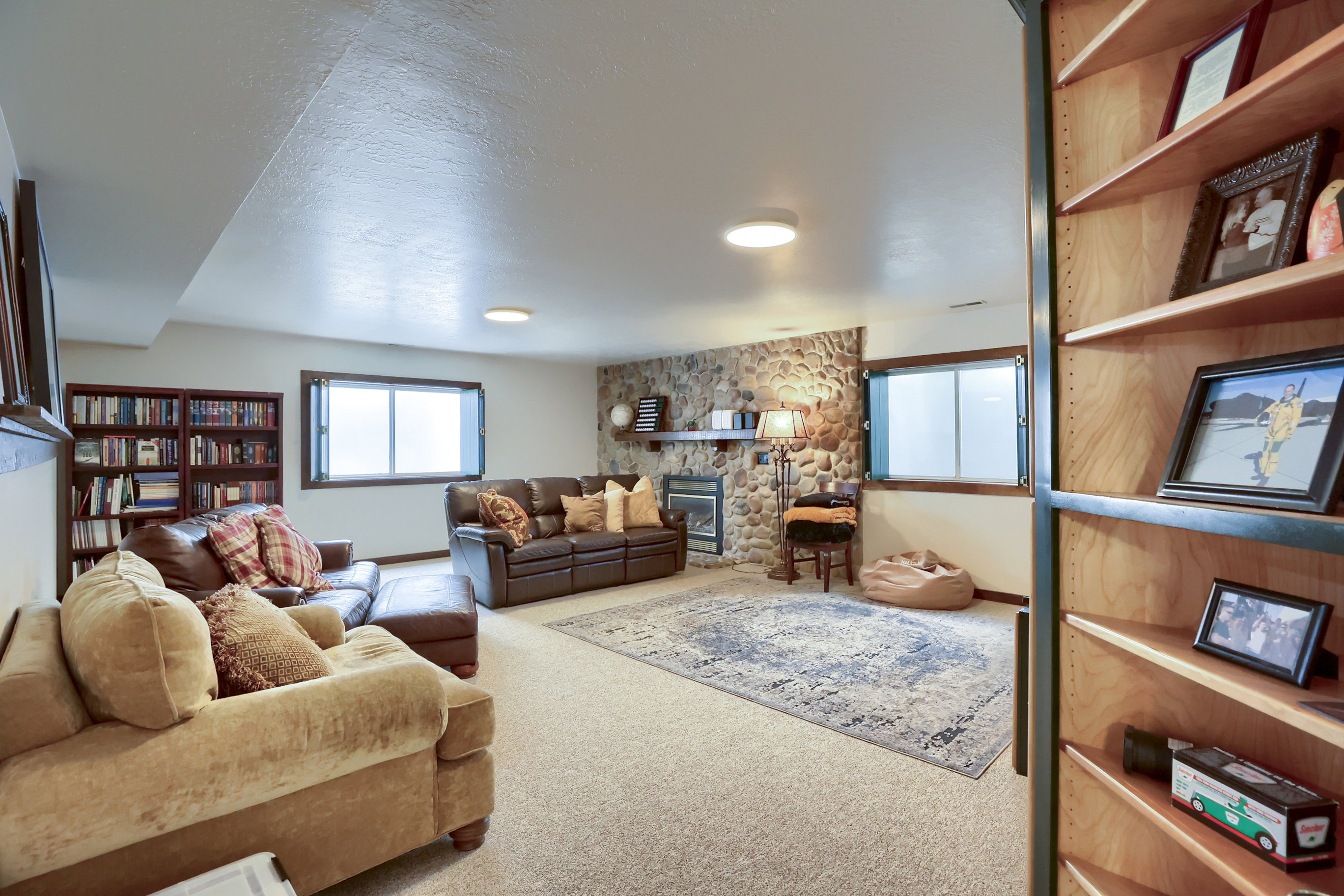 Spacious lower level featuring a stone-clad fireplace, built-in shelving, two egress windows, and recessed lighting