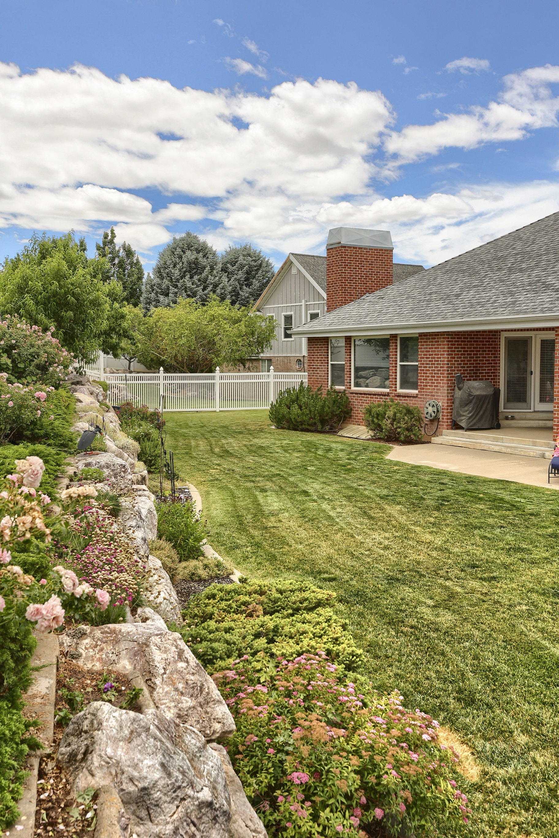 Spacious backyard featuring a manicured lawn, an expansive rock garden, and a white privacy fence