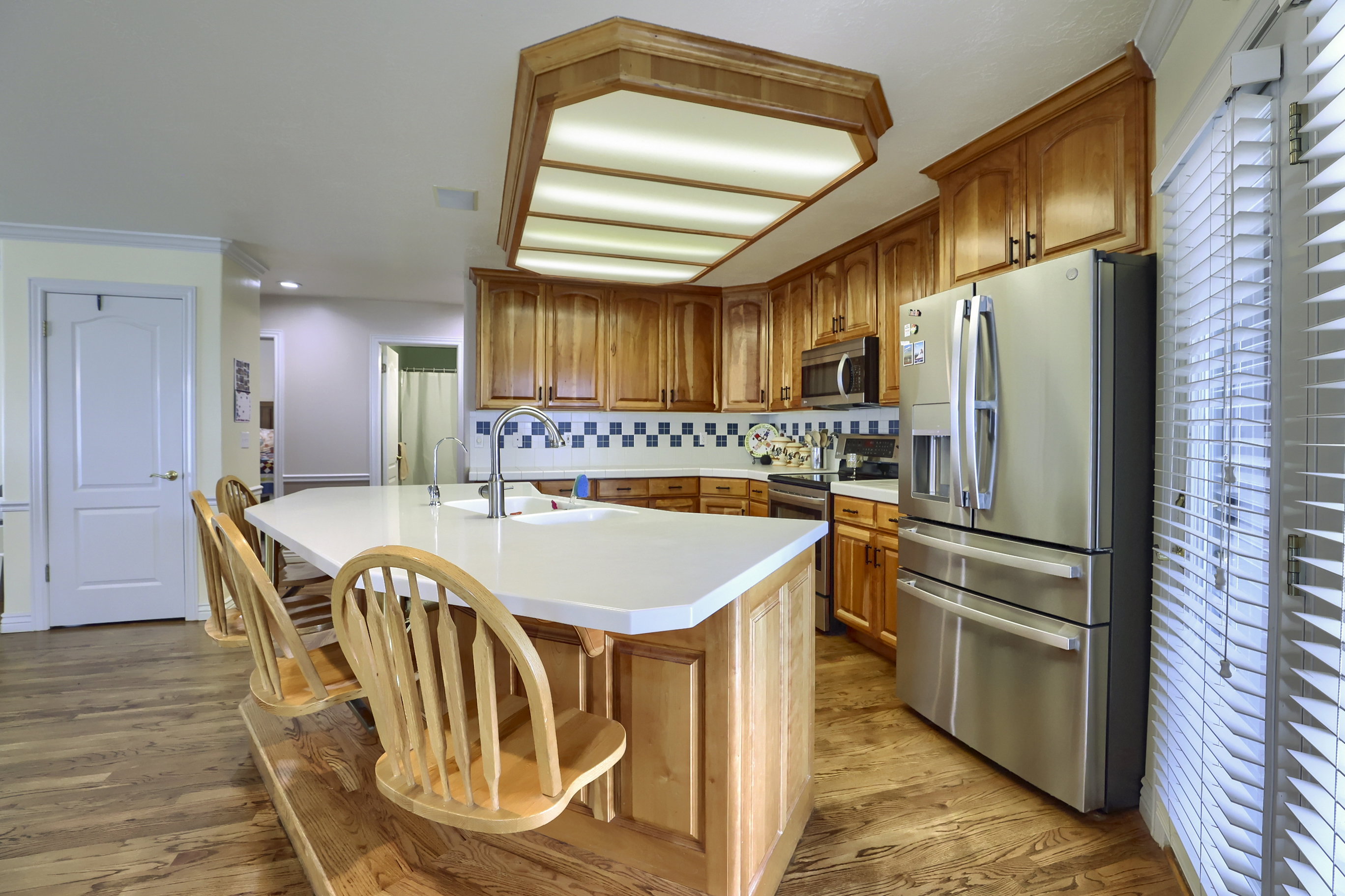 Expansive kitchen featuring wood-finish flooring, custom wood cabinetry, stainless steel appliances, a center island with a solid surface countertop, and an integrated ceiling light fixture