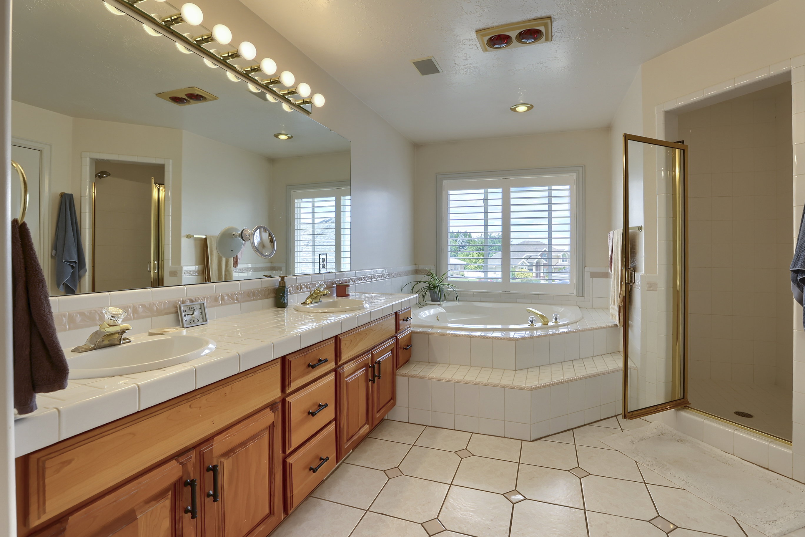 Bathroom featuring a built-in corner soaking tub, a dual vanity with tile countertop, wood cabinetry, and a glass-enclosed shower