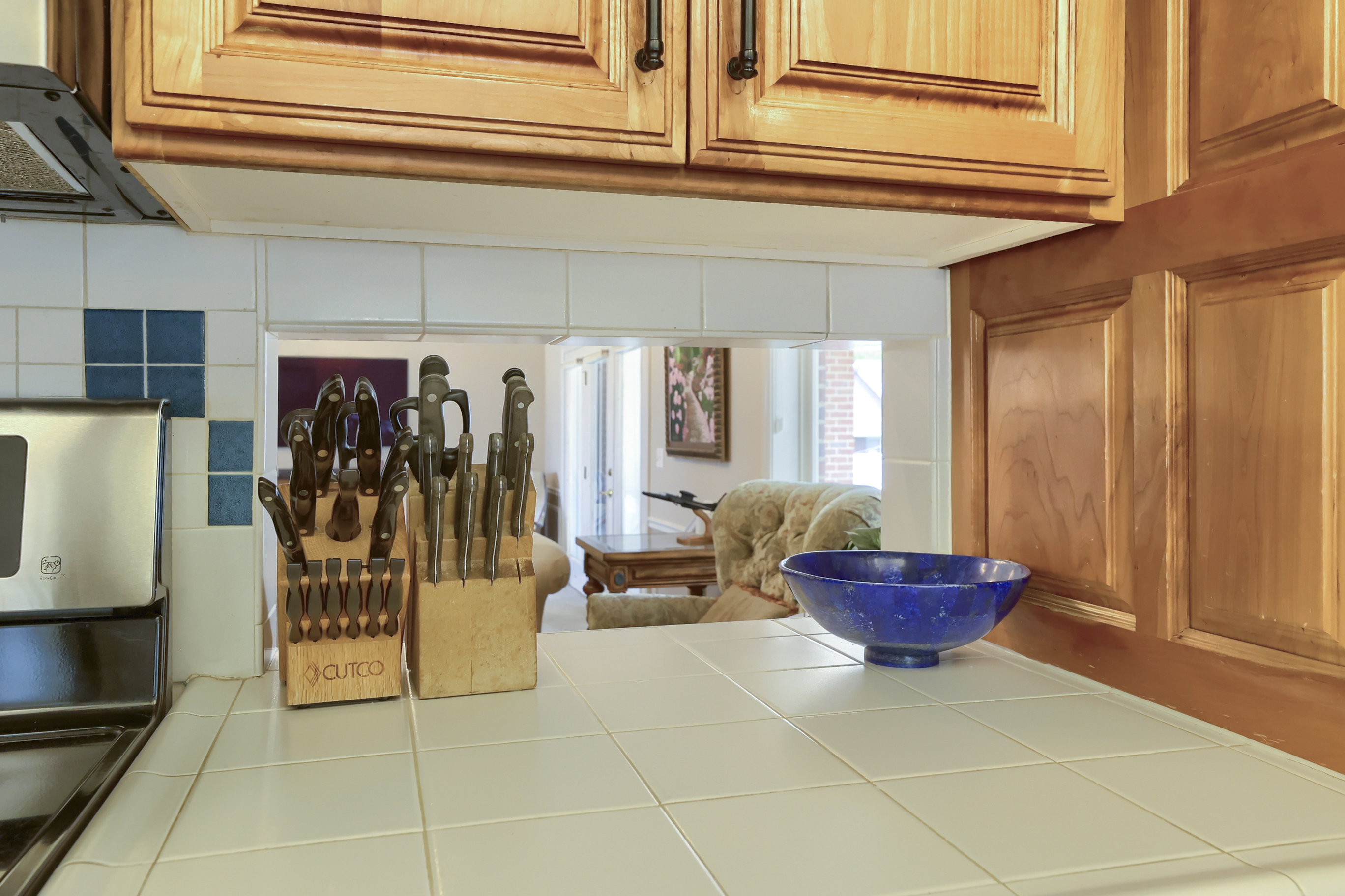 Kitchen featuring light wood cabinetry, white tile countertops, and a white tile backsplash with blue accents