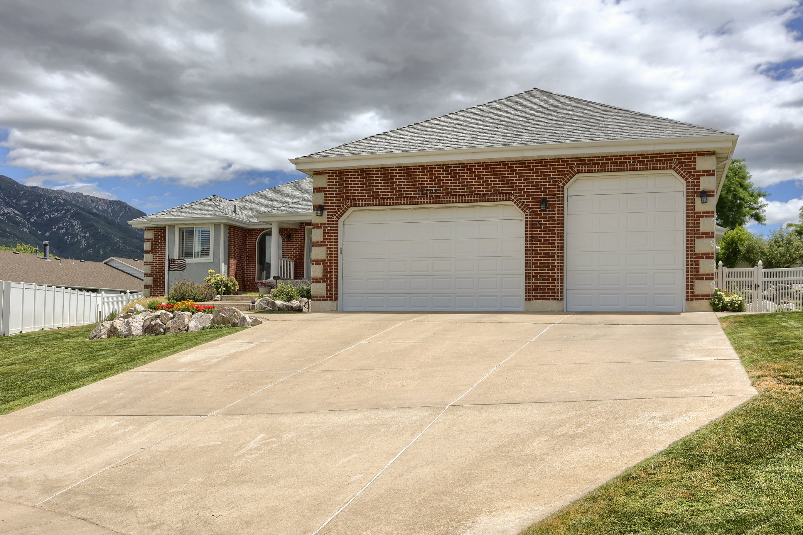 Brick exterior with a three-car garage, concrete driveway, and front landscaping featuring rockery and plantings