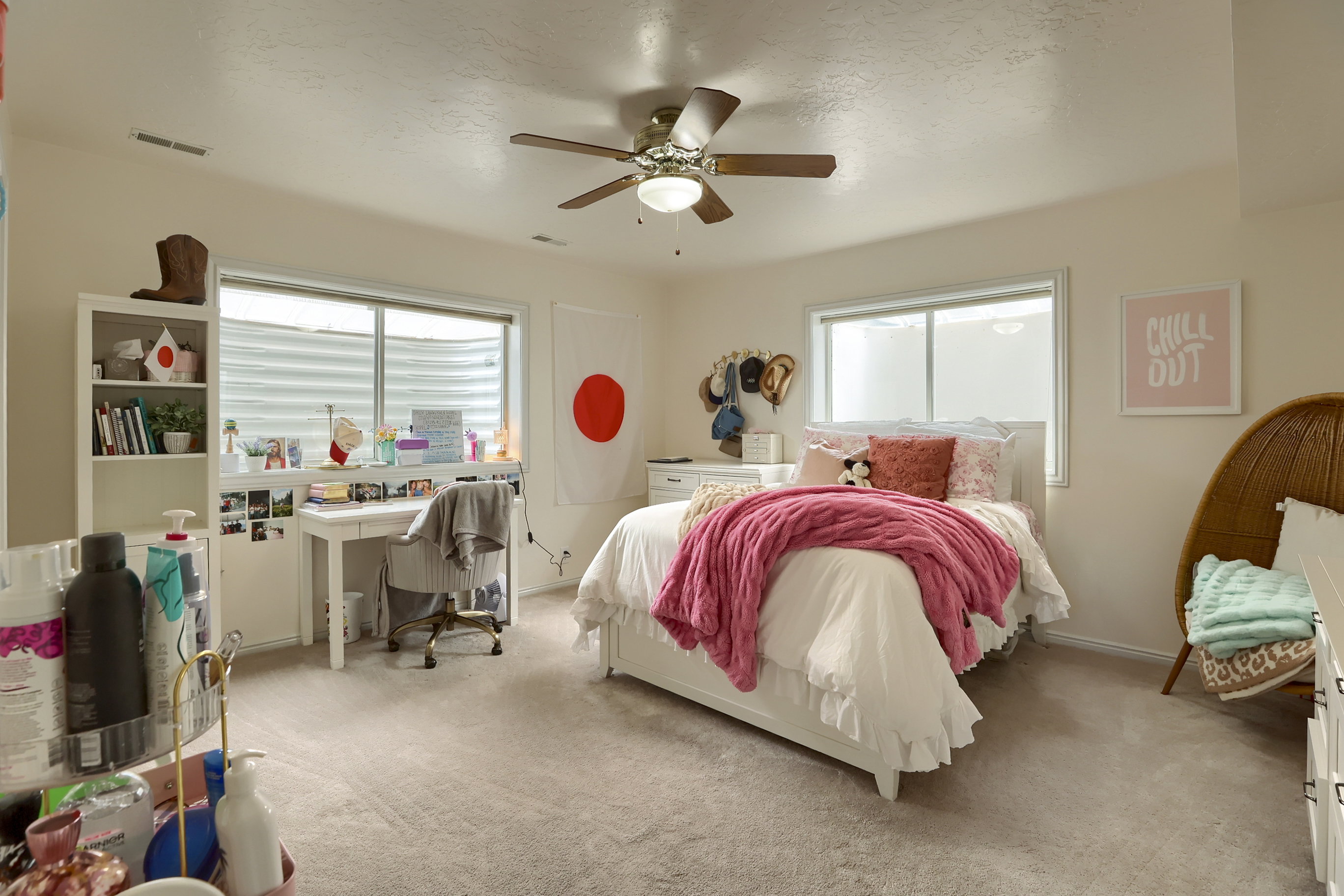 Carpeted room featuring a ceiling fan, dual windows, and built-in shelving