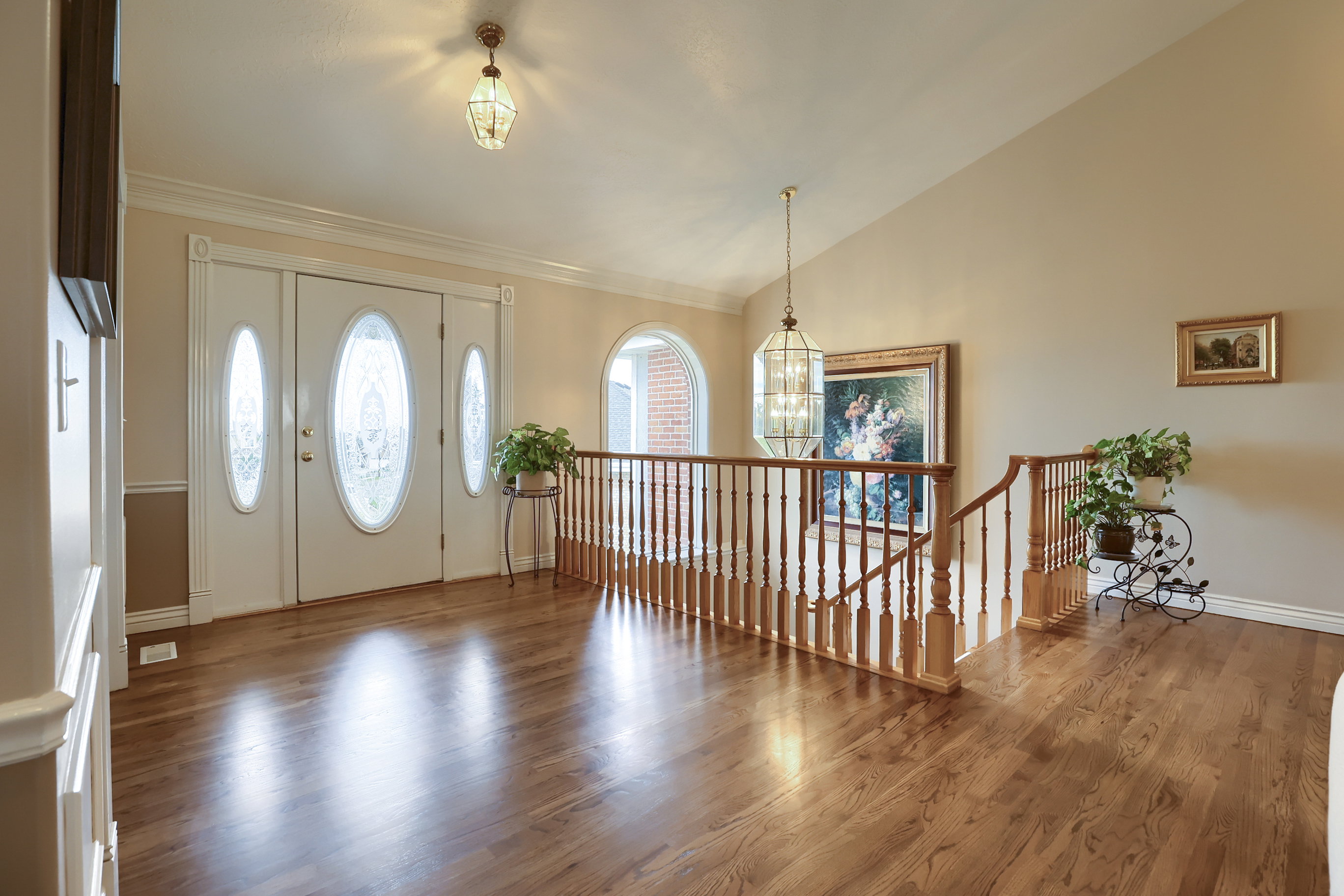 Double entry doors with decorative oval glass inserts, polished wood-finish flooring, a wood banister, a vaulted ceiling, and an arched window