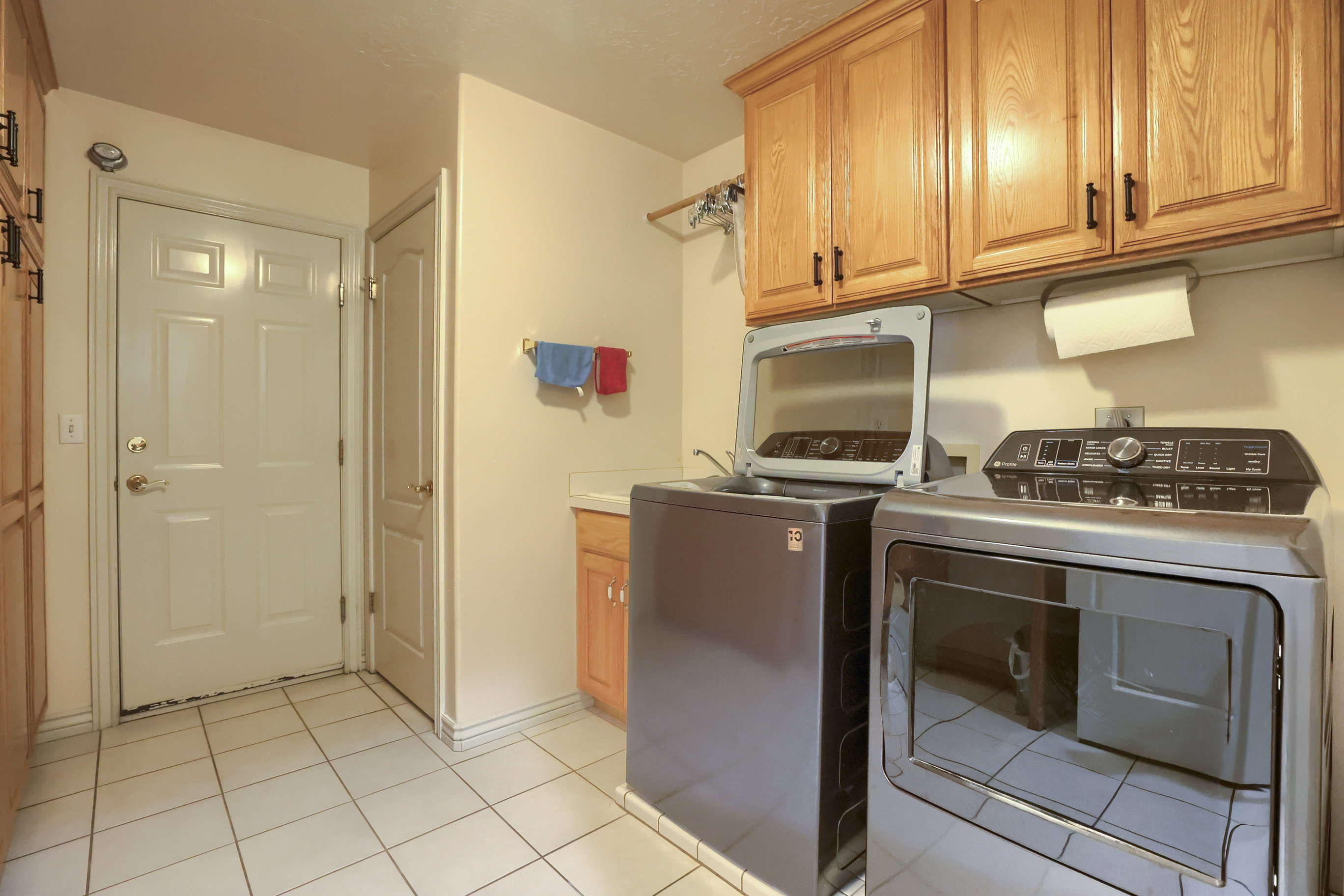 Laundry room featuring a white paneled door, tile flooring, and light wood cabinetry with dark hardware