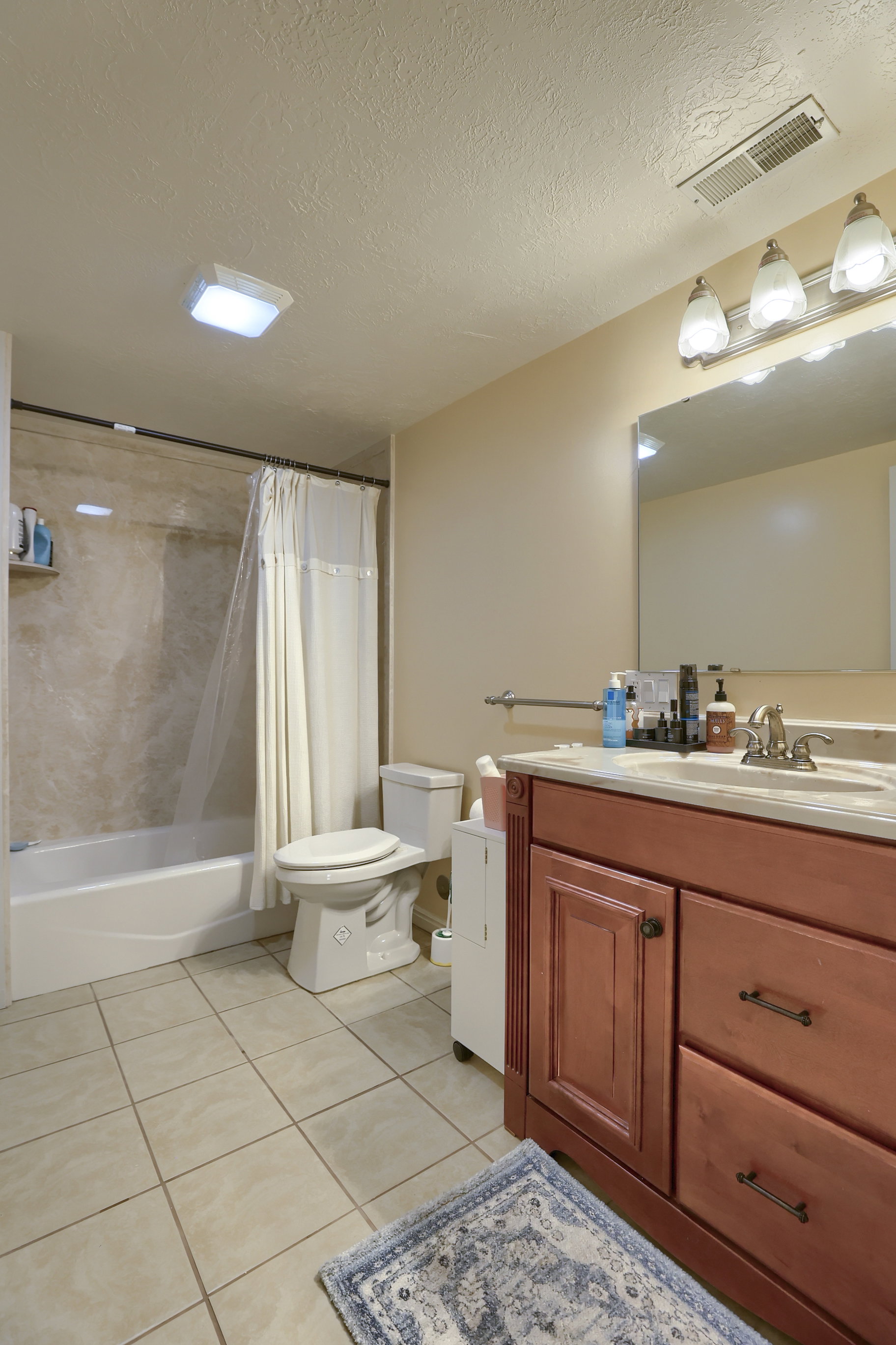 Bathroom featuring a wood-finish vanity with a light-toned countertop, a shower-tub combination with a tiled surround, and large format floor tiling