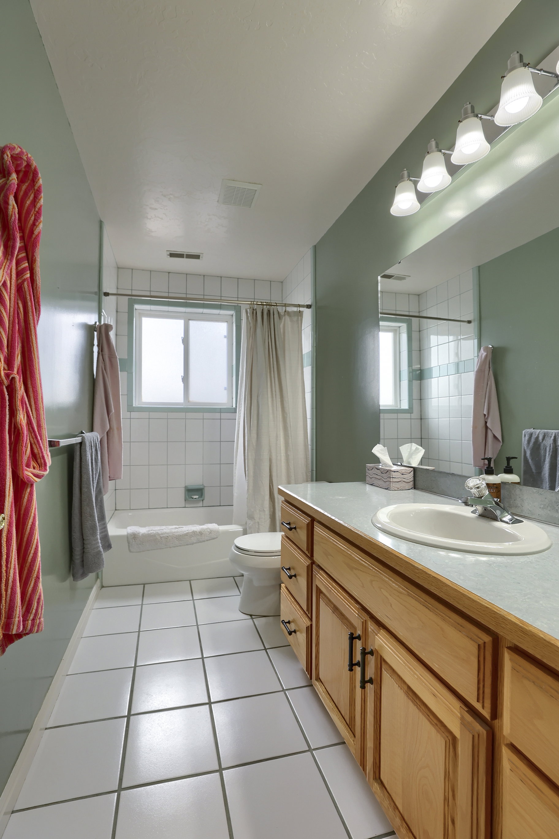 Bathroom featuring a wood-finish vanity with an integrated sink, a large mirror, and a four-bulb vanity light fixture