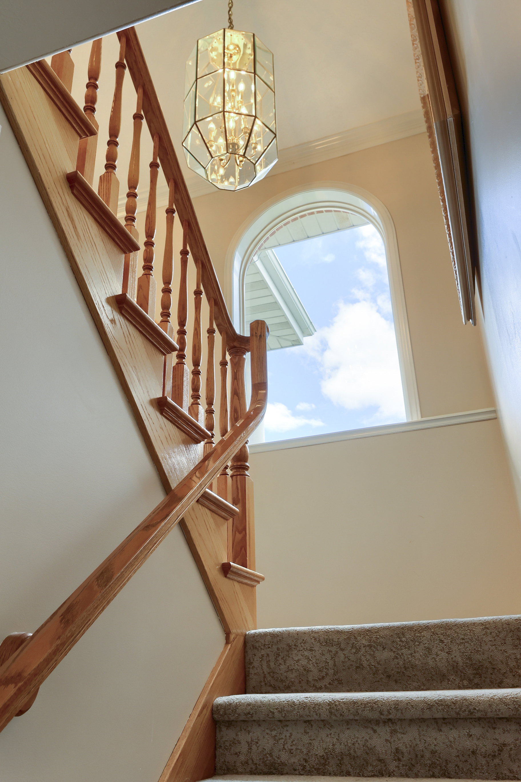 Carpeted staircase with light wood banister and spindles, illuminated by a decorative glass chandelier