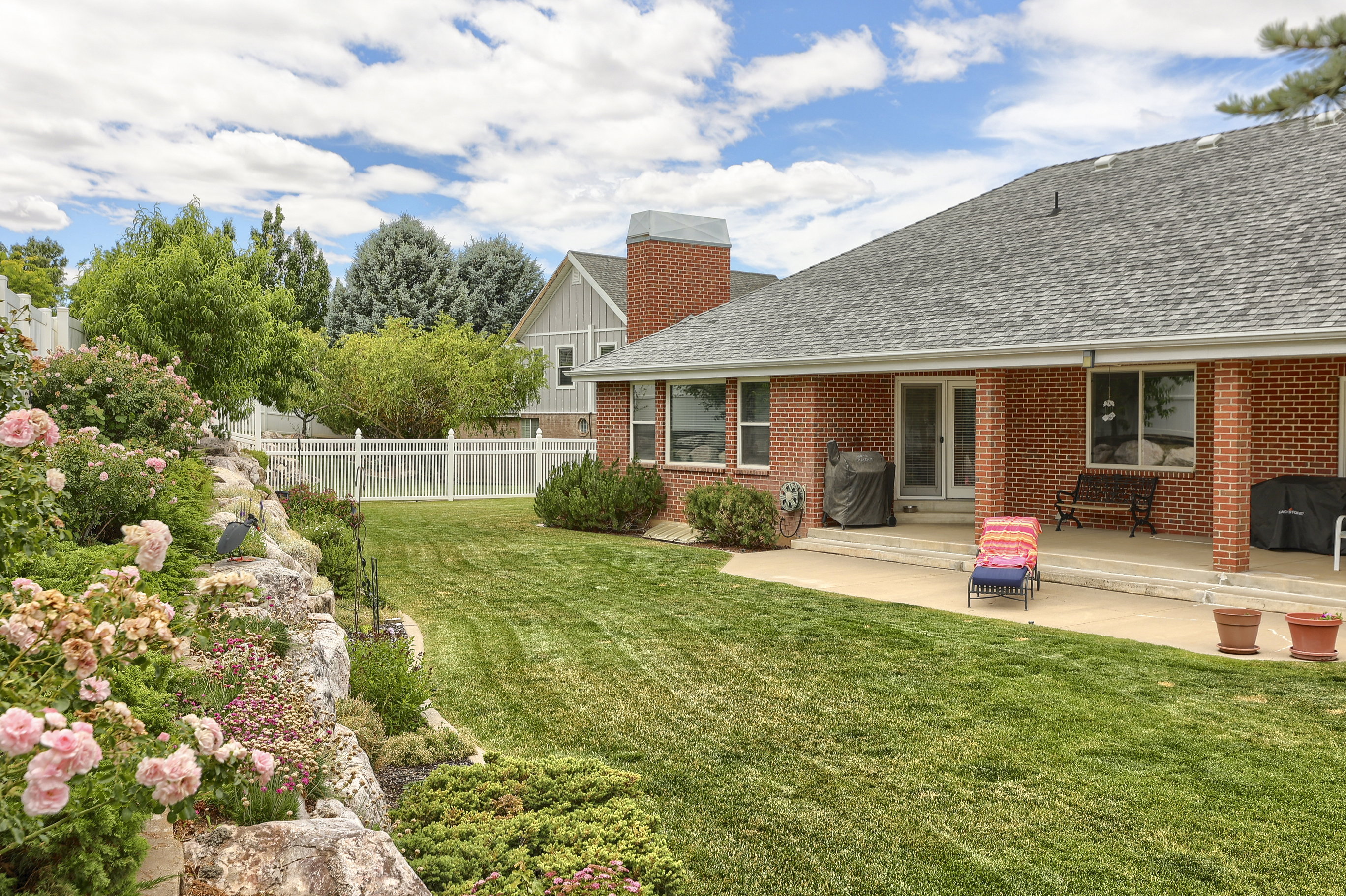 Expansive backyard featuring a manicured lawn, a rock garden with flowering shrubs, and a white picket fence