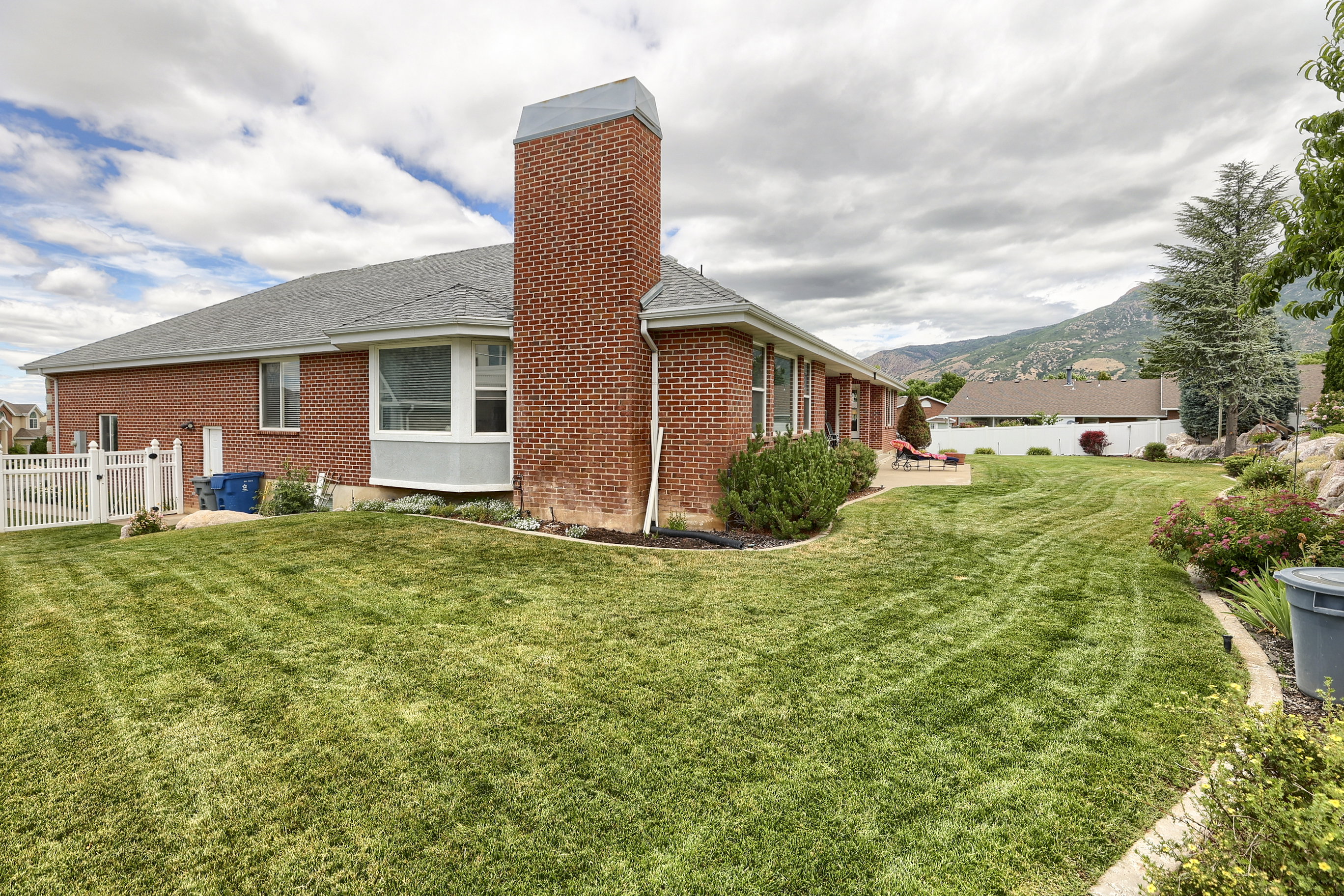Expansive lawn area featuring a paved patio, red brick exterior, bay window, and surrounding landscaping
