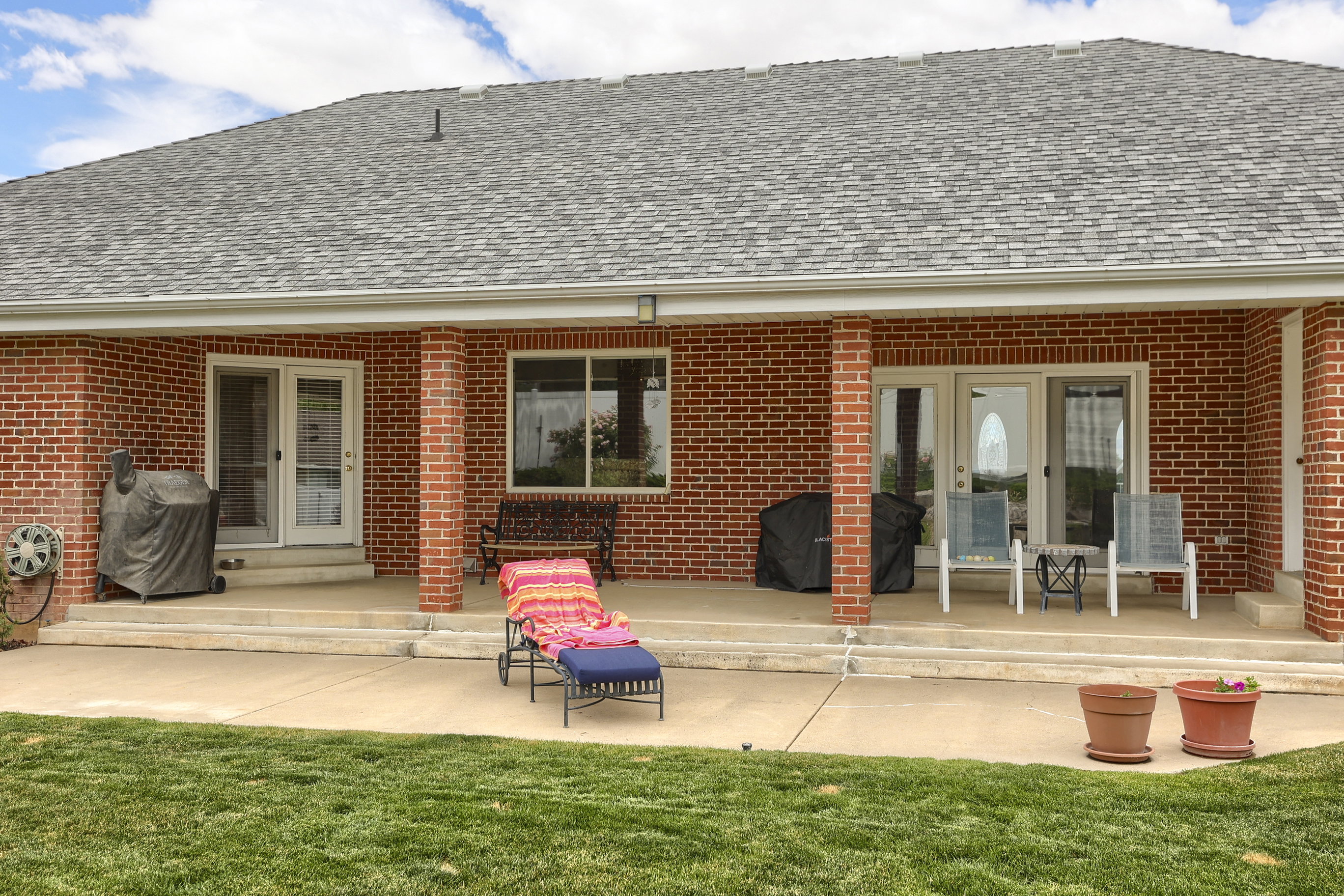 Covered patio featuring brick columns, red brick exterior, and a shingle roof