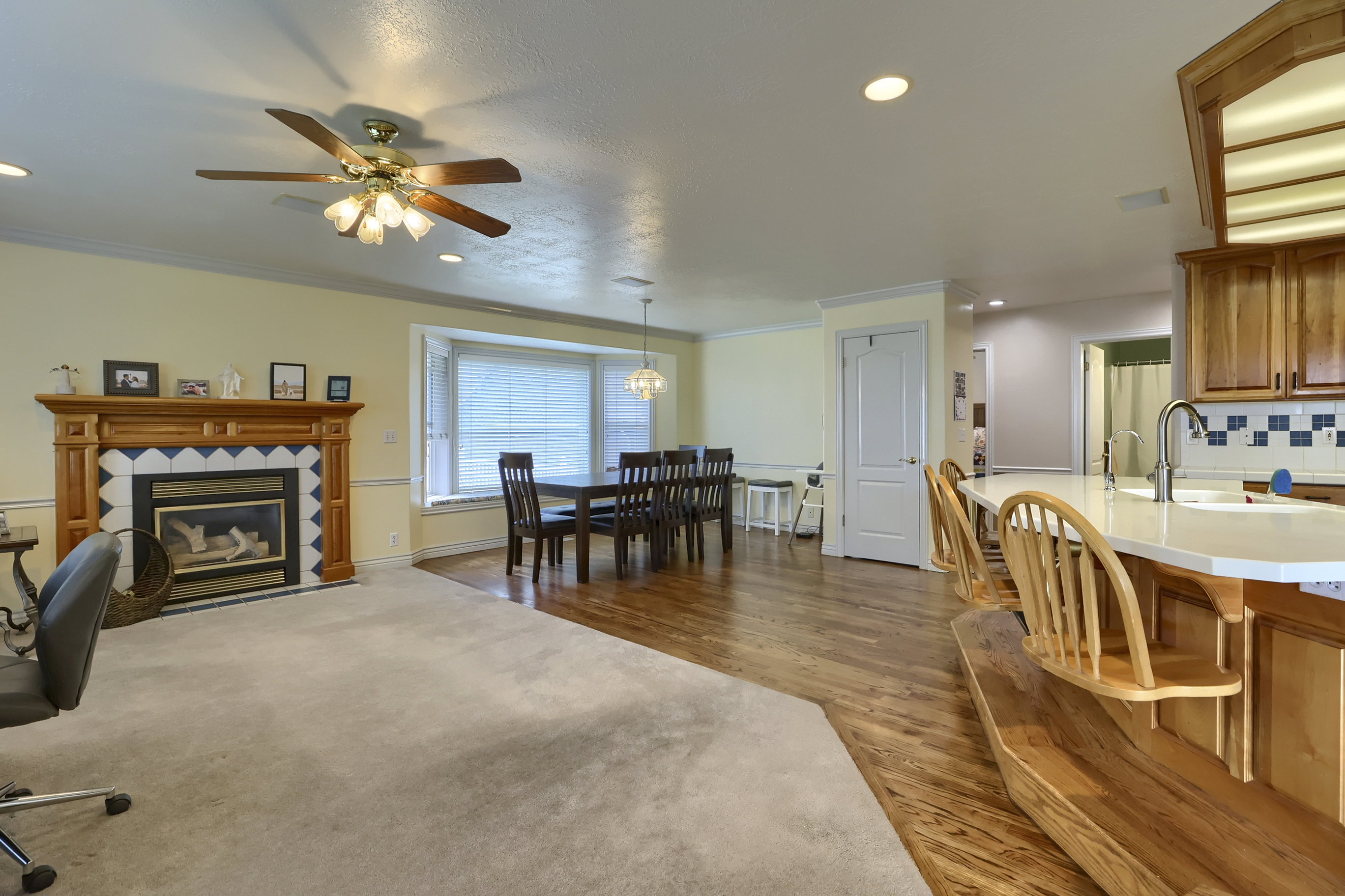 Integrated living and dining space featuring a fireplace with a wood mantle and tile surround, a bay window, and a kitchen island with seating