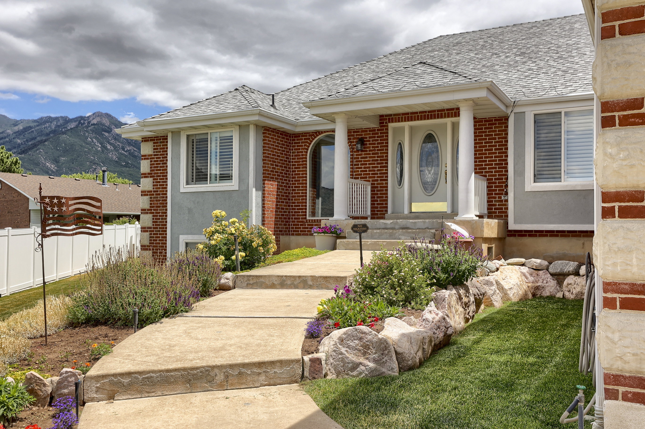 Brick and stucco exterior featuring a columned entryway, arched transom window, and a gray shingle roof