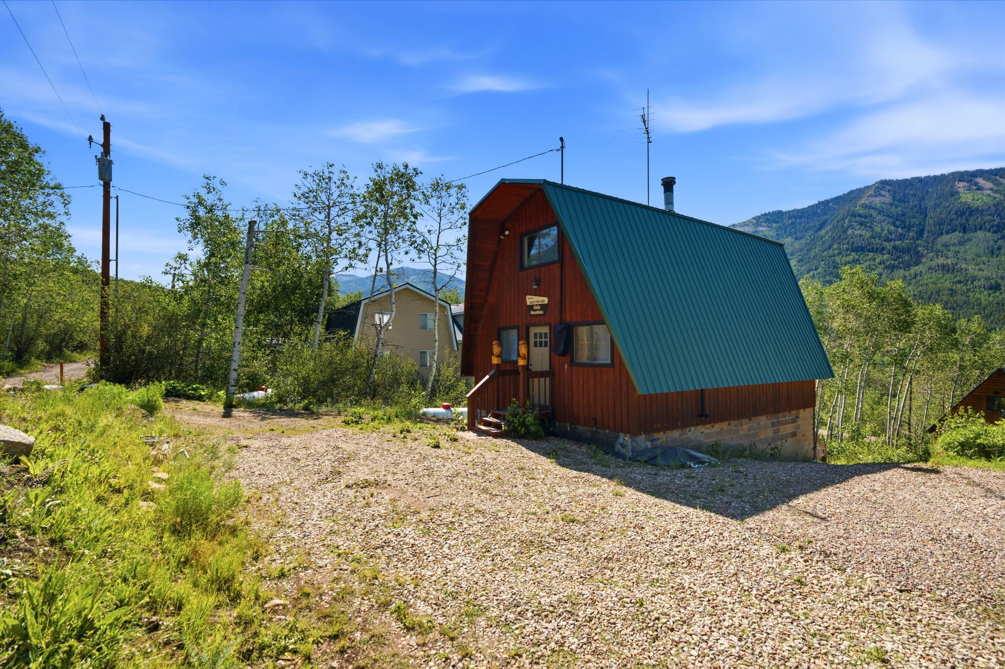 A-frame structure featuring wood siding, a green metal roof, and a gravel parking area