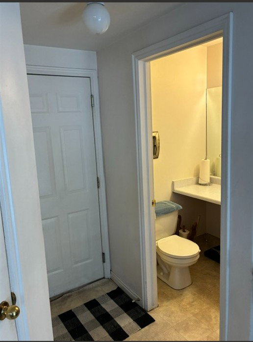Interior doorway opening to a bathroom featuring a commode and a vanity with an integrated sink and mirror