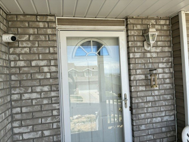 Exterior entry featuring brick facade, white storm door with arched window, and outdoor wall lantern