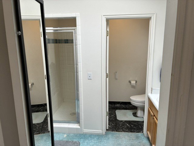 Bathroom featuring a walk-in shower with glass enclosure, white tile surround, and a black accent tile band