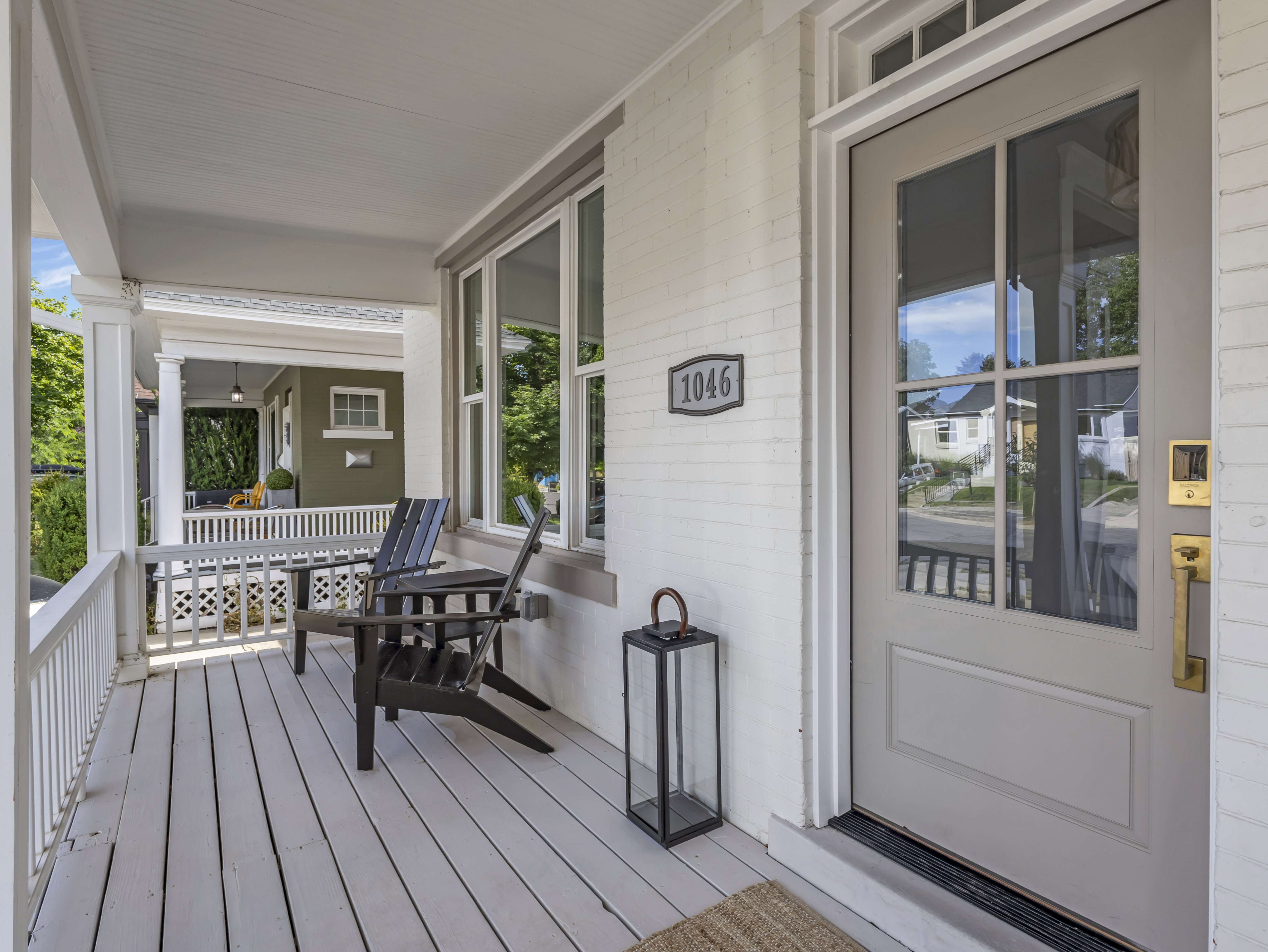 Inviting front porch featuring painted wood flooring, white railings, and a contrasting brick facade