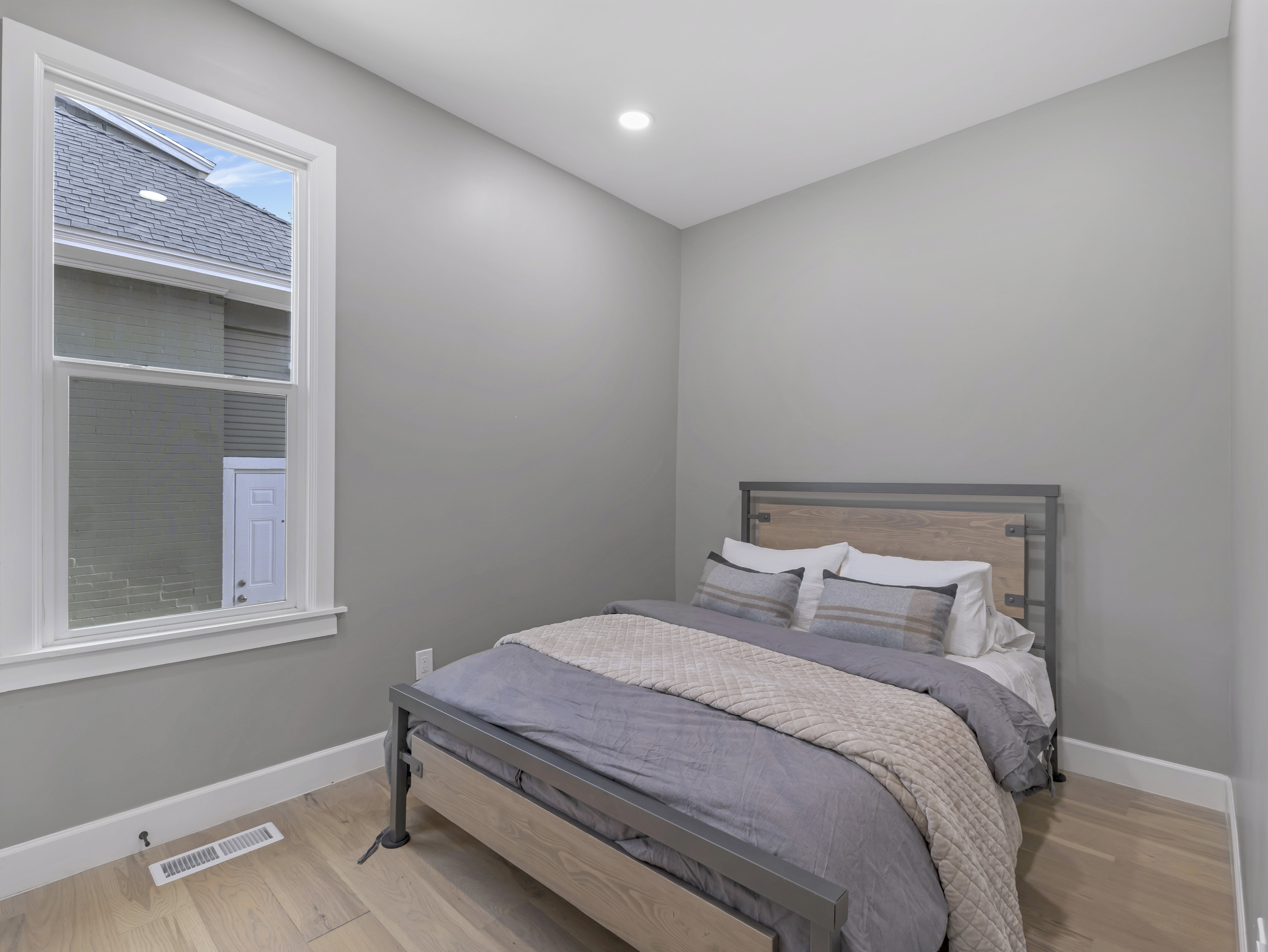 Light-filled bedroom featuring wood-finish flooring, a white trim window, neutral wall paint, recessed ceiling lighting, and crisp white baseboards