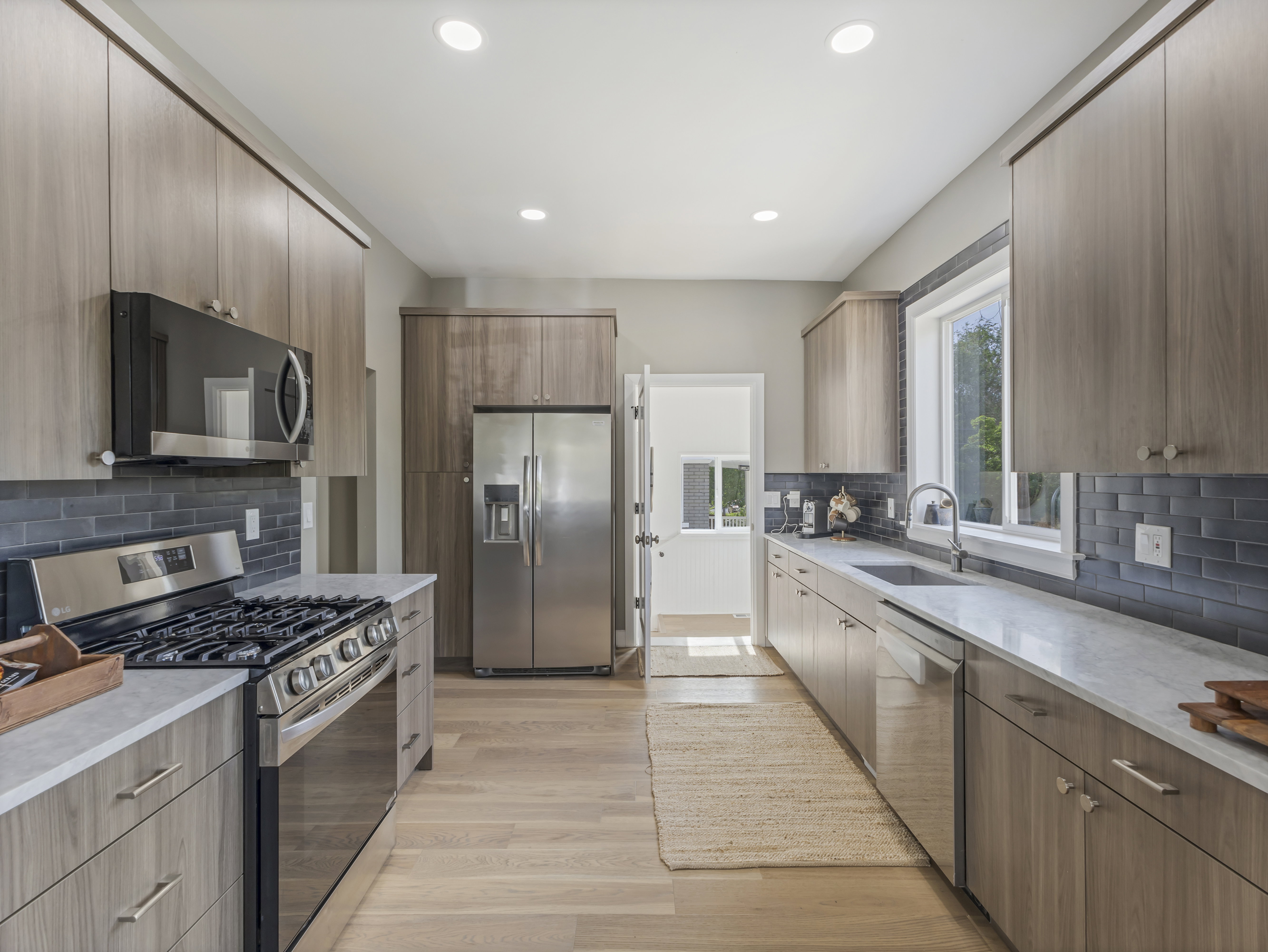 Modern galley kitchen featuring light wood-finish cabinetry, stainless steel appliances, a subway tile backsplash, and recessed lighting